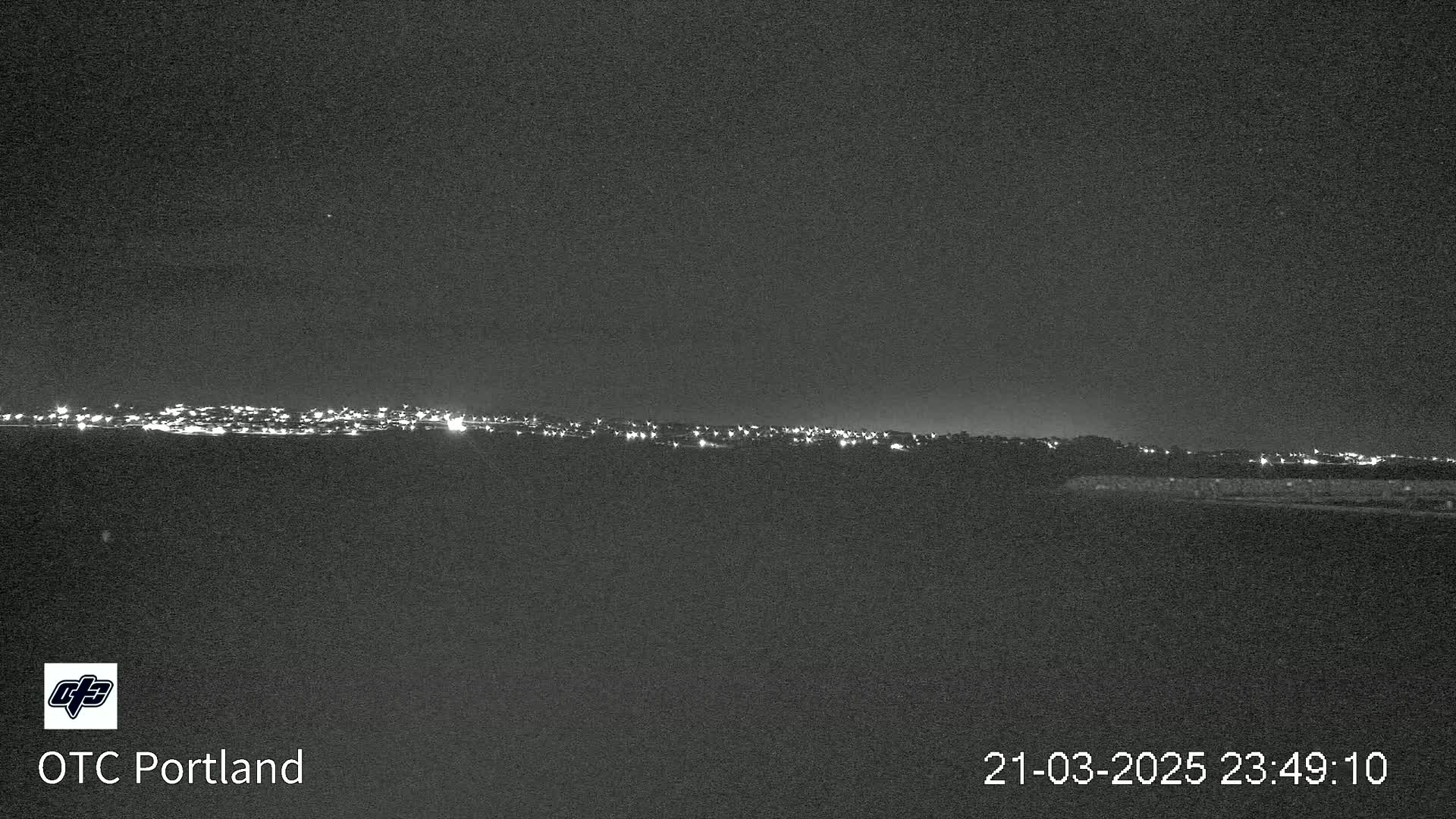 A nighttime long shot reveals a distant cityscape illuminated by numerous lights under a clear, dark sky.