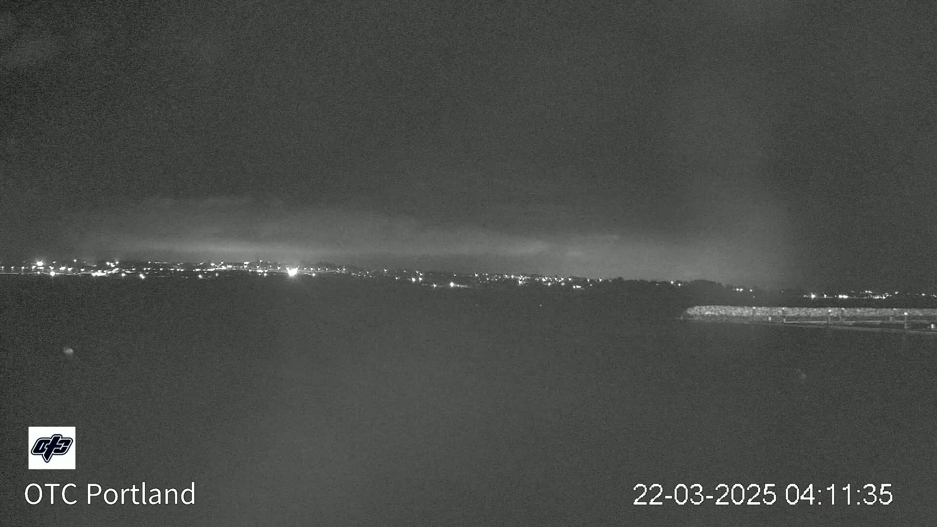 A nighttime long shot shows a distant cityscape with a low cloud cover under a dark sky.