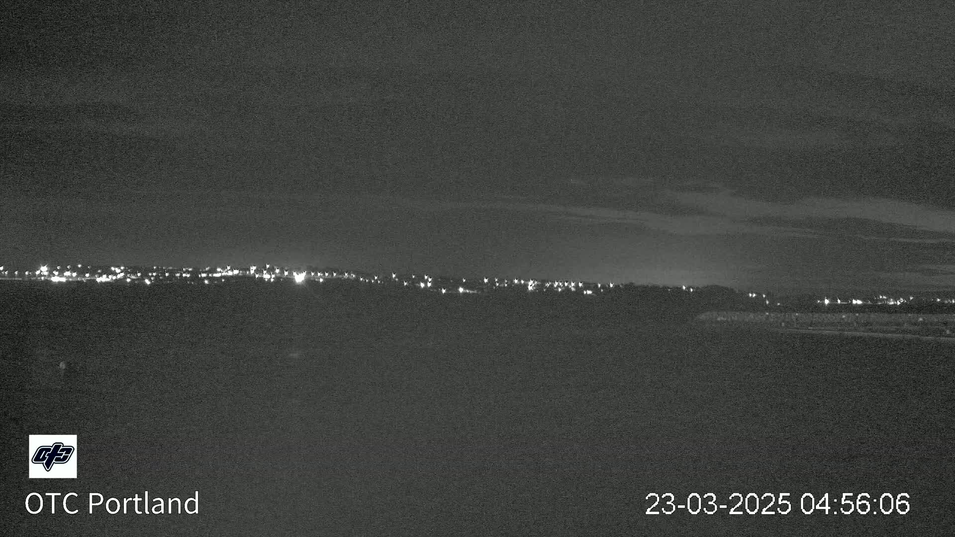 A nighttime long shot shows a distant line of city lights under a mostly clear sky.