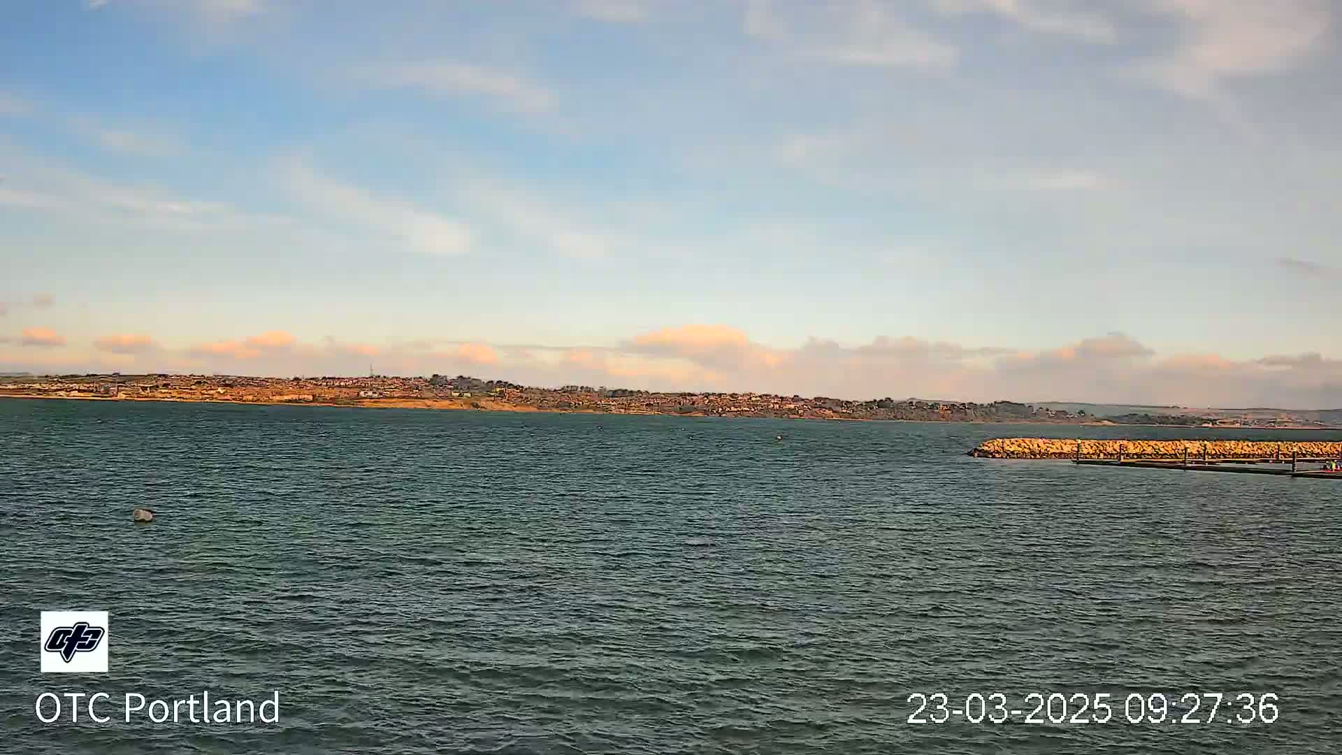 A calm body of water stretches out to a distant shoreline under a partly cloudy sky.
