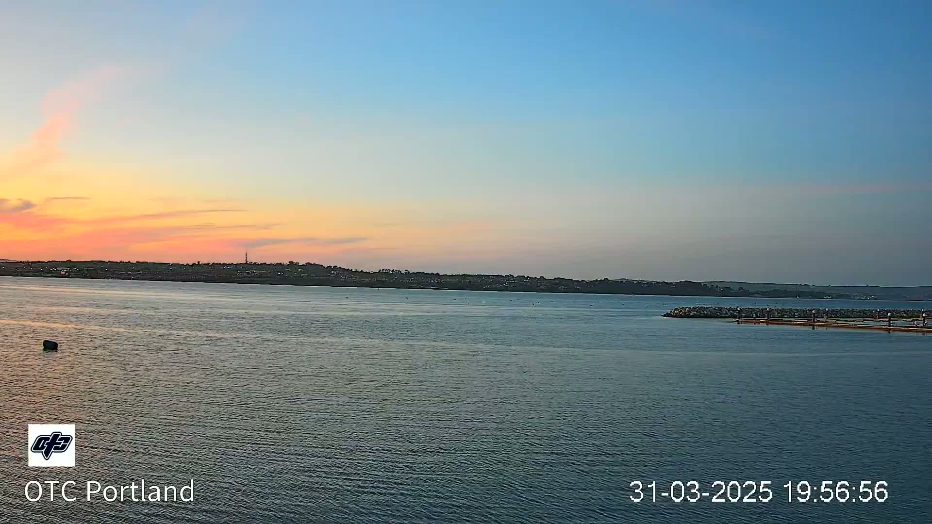 A calm body of water shows a pastel sunset over a distant shoreline.