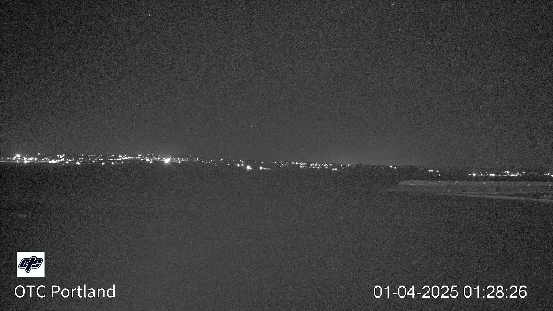 A nighttime long shot shows a distant city skyline illuminated by faint lights under a clear, dark sky.