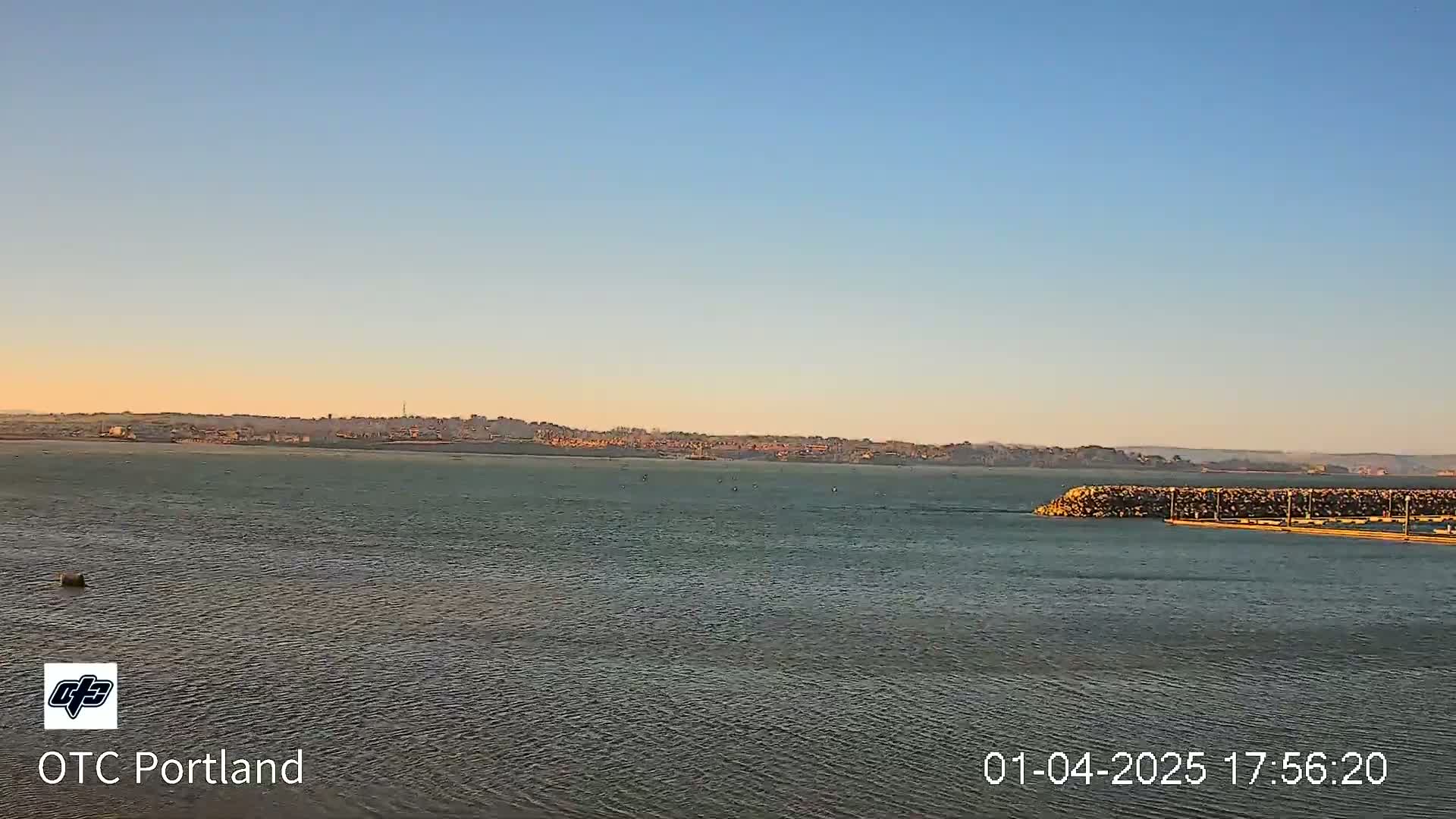 A calm body of water stretches to a distant cityscape under a clear, twilight sky.