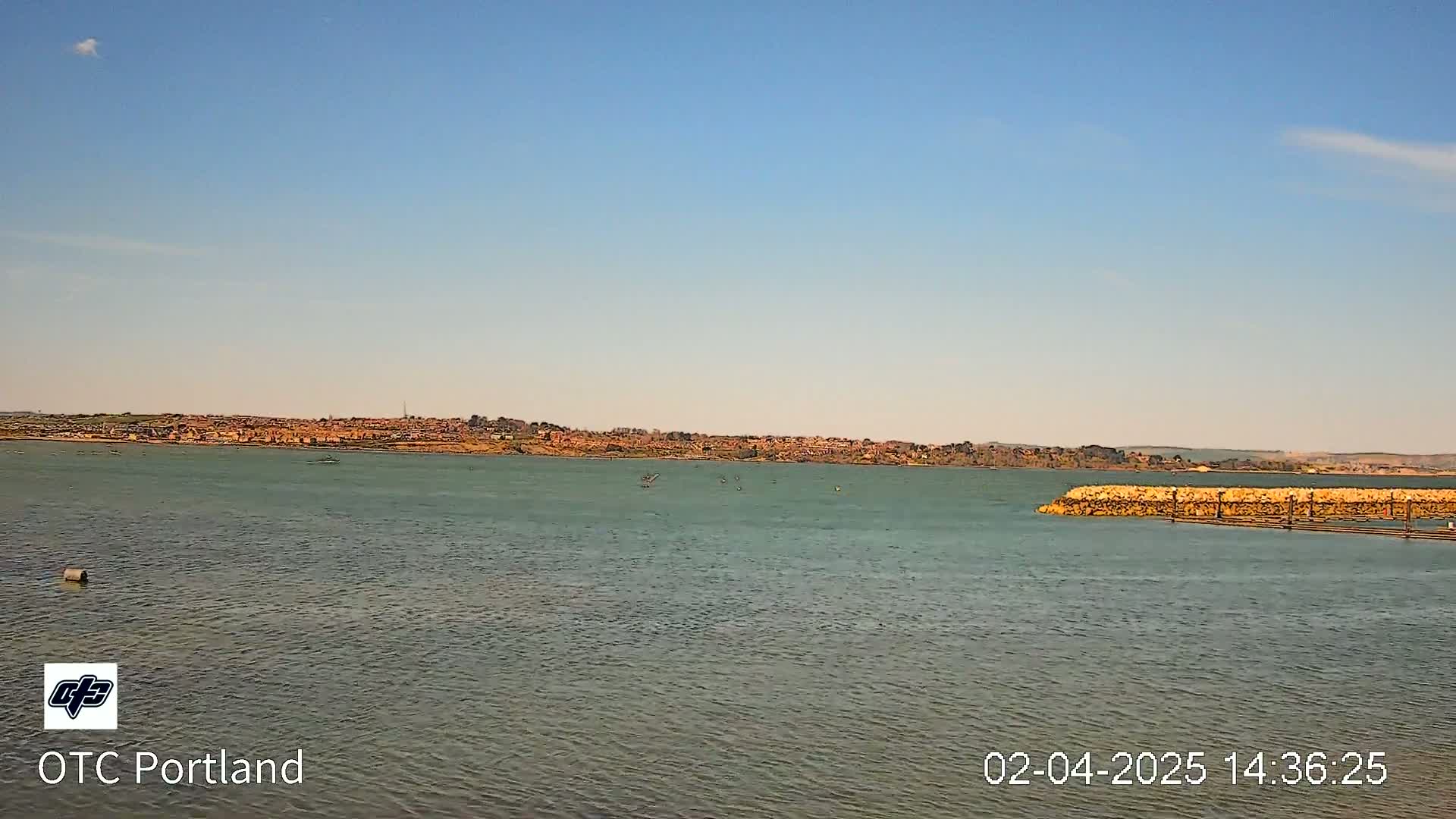 A calm body of water stretches toward a distant town under a clear blue sky.