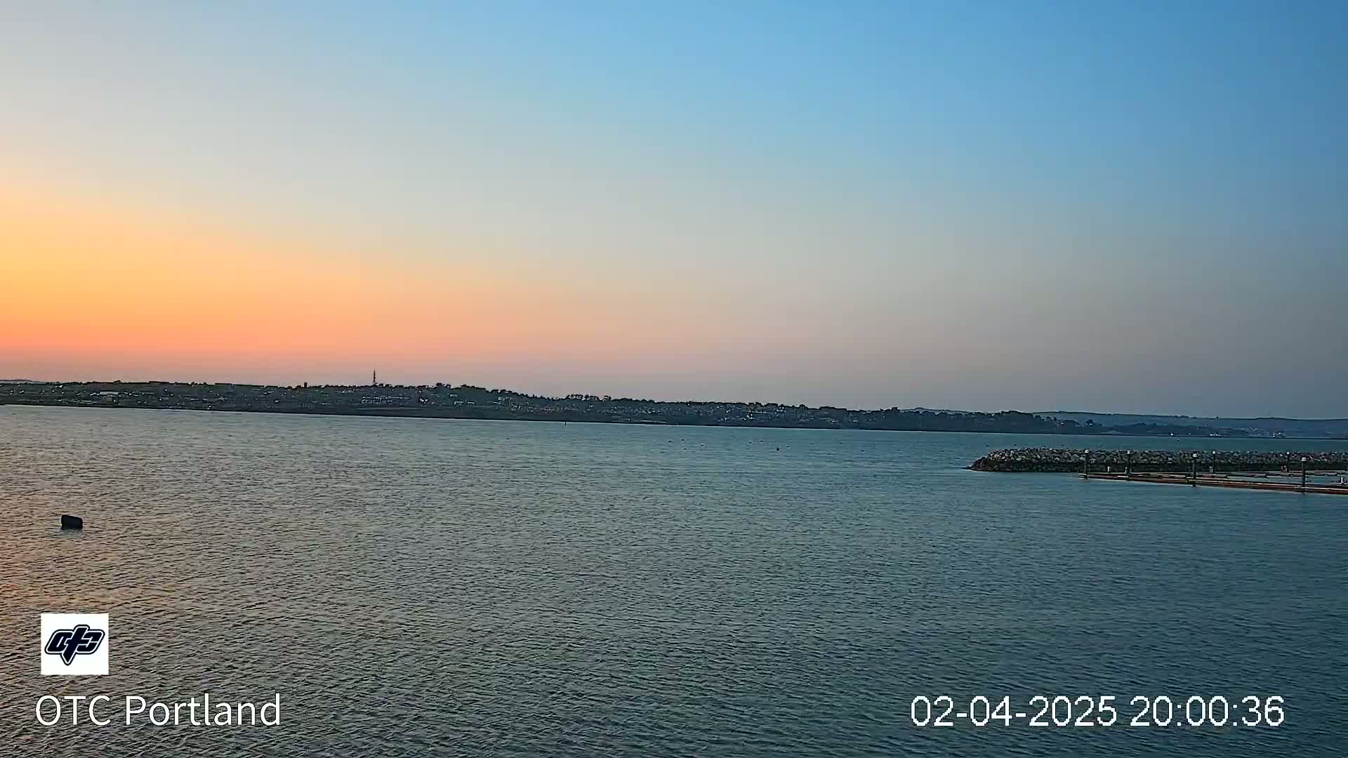 A calm body of water shows a sunset over a distant shoreline.