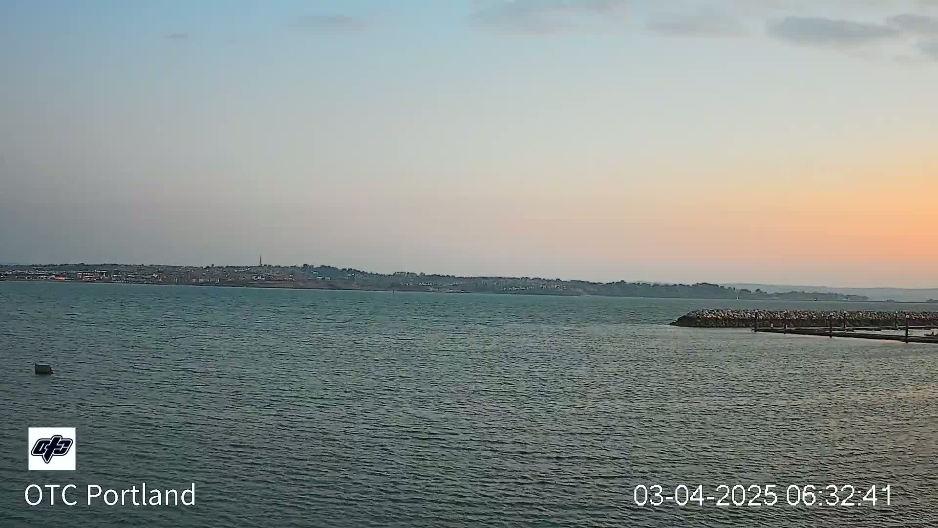 A calm body of water shows a distant shoreline under a pale, sunset sky.