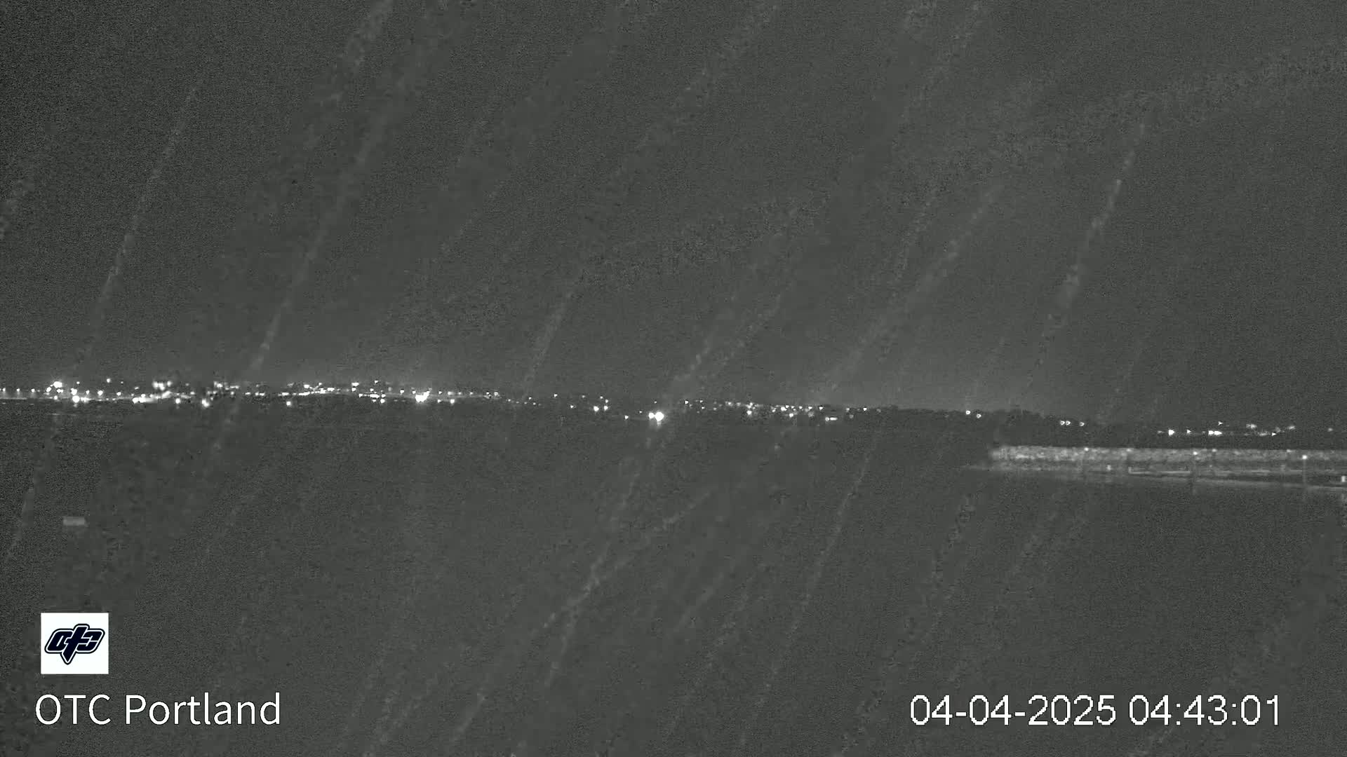 A nighttime long shot shows a distant line of city lights under a dark, possibly rainy, sky.