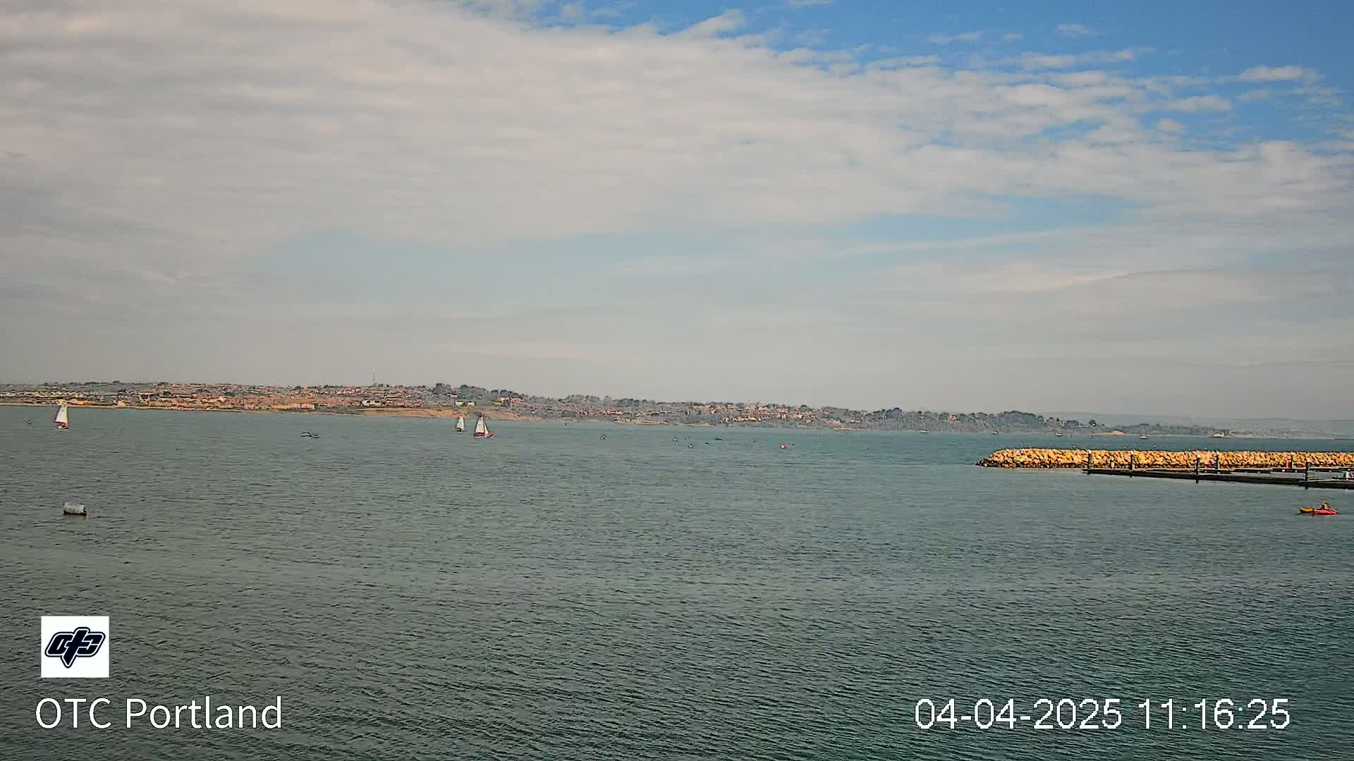 A calm body of water with a few sailboats and a distant shoreline under a partly cloudy sky.