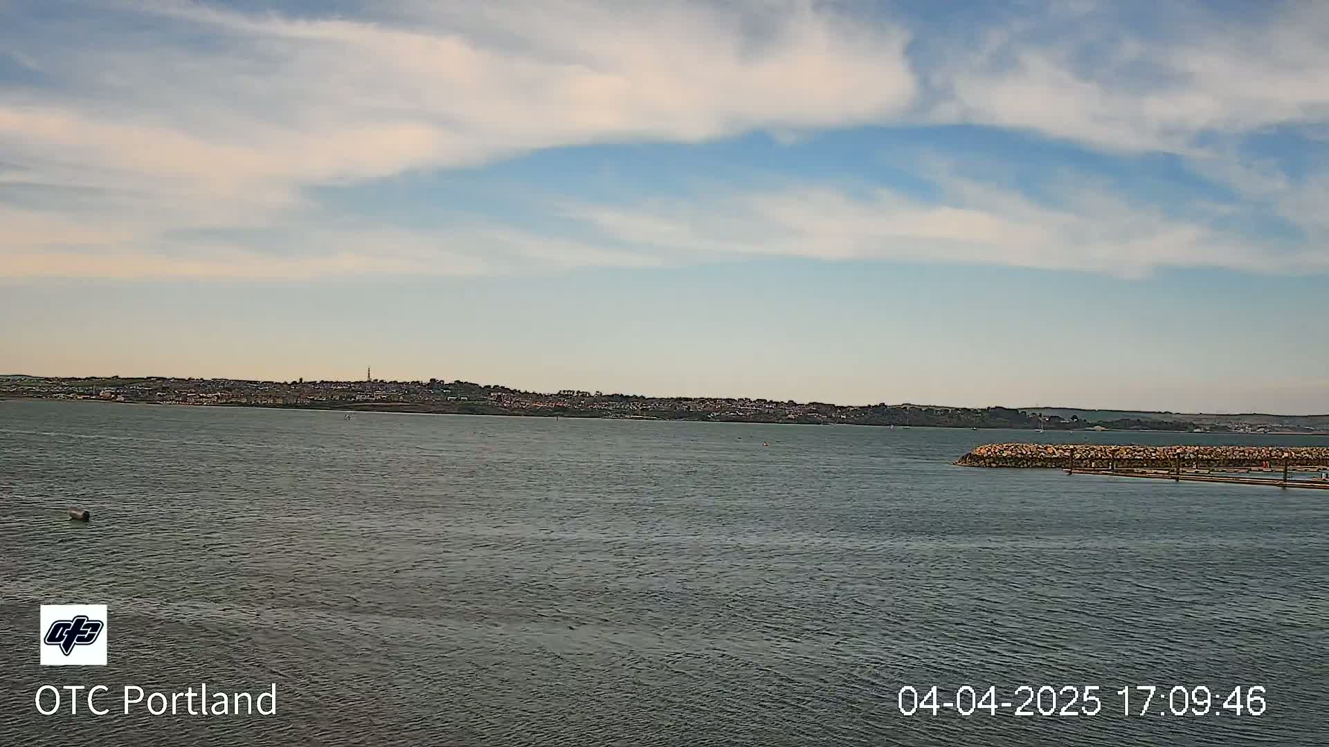 A calm body of water shows a distant town under a partly cloudy sky.