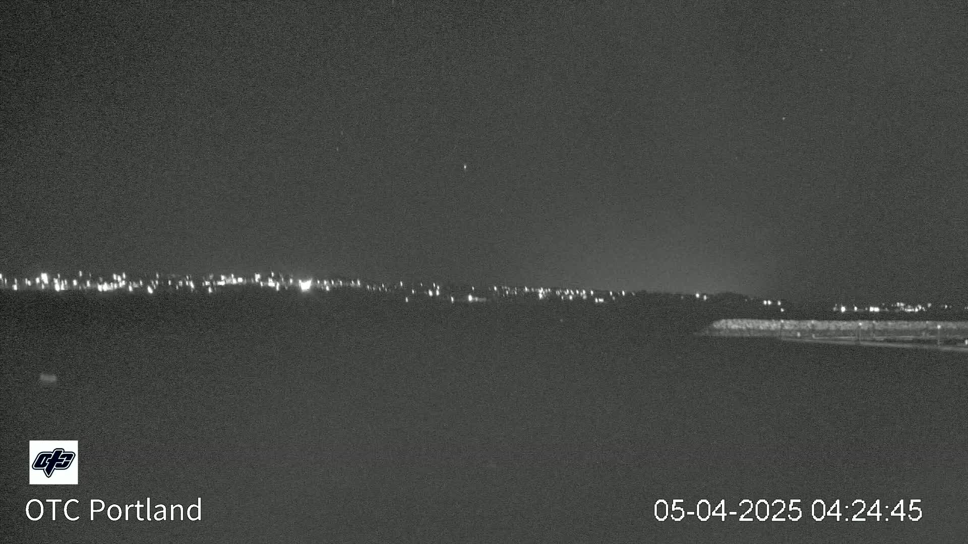 A nighttime long shot shows a distant line of city lights under a clear, dark sky.