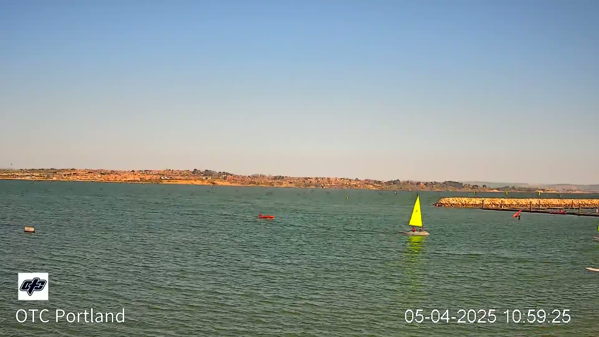 A calm body of water with several small sailboats and a distant shoreline under a clear, bright sky.