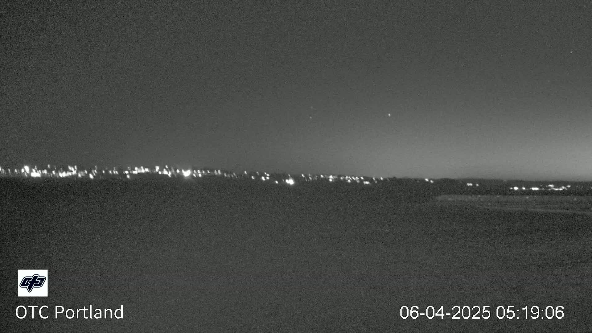 A nighttime long shot of a distant city skyline with faint lights under a dark sky.