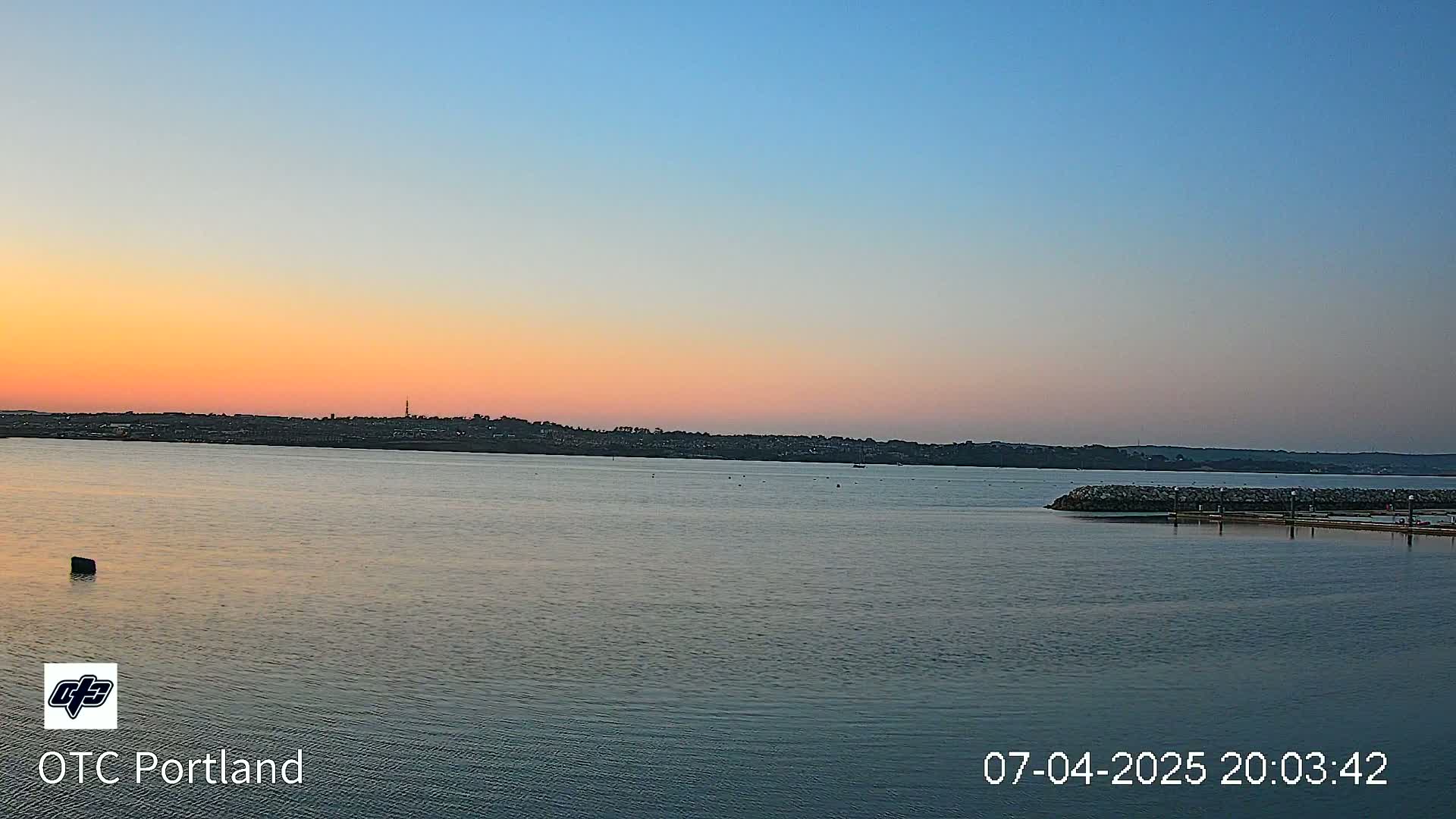 A calm body of water at sunset shows a distant shoreline under a mostly clear sky.