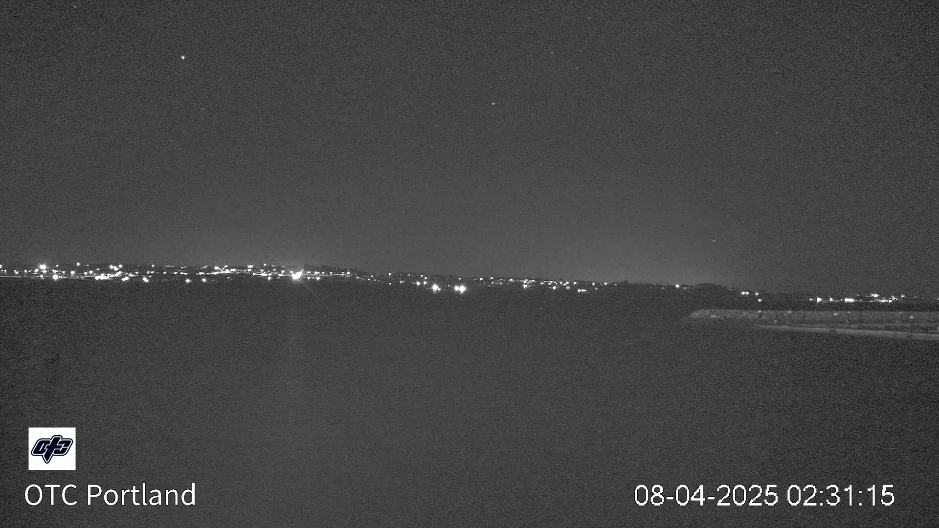 A nighttime view shows a distant city skyline with faint lights under a clear, dark sky.
