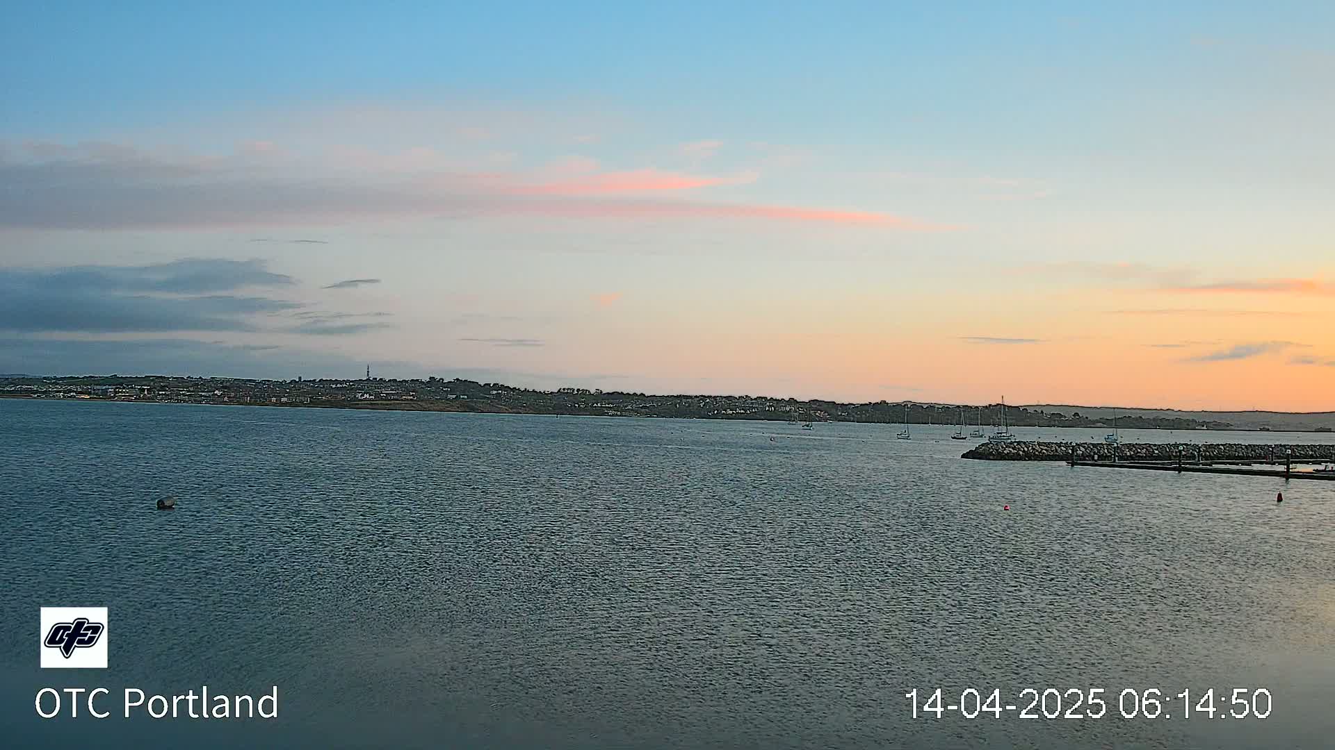 A calm body of water with a distant shoreline under a pale pink and blue sunset sky.