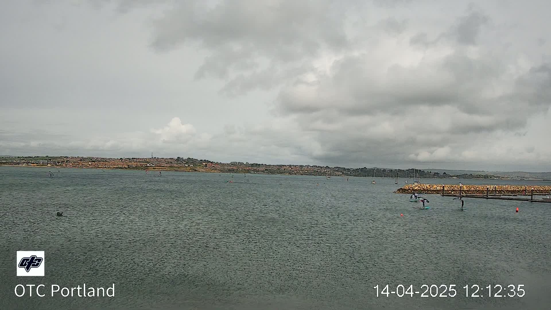 A body of water with several people on paddleboards under an overcast sky.