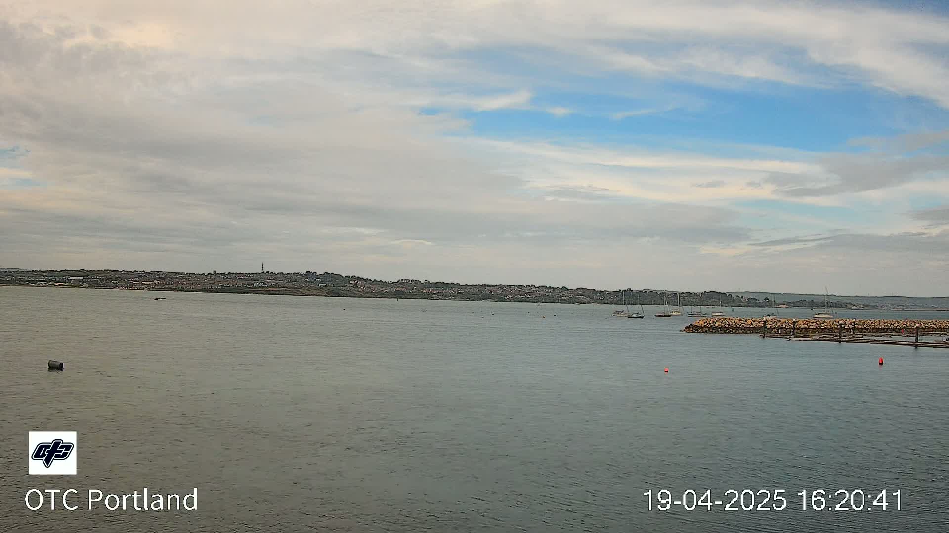 A calm body of water shows a distant town under a partly cloudy sky.