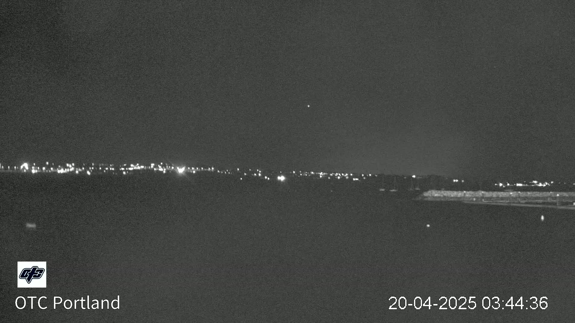 A nighttime long shot shows a distant line of city lights under a clear, dark sky.