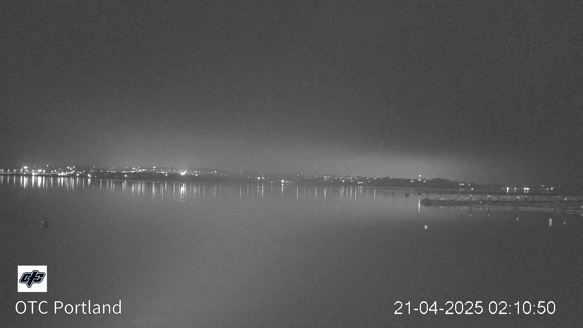 A nighttime view of a calm body of water reflecting the lights of a distant city under a dark sky.