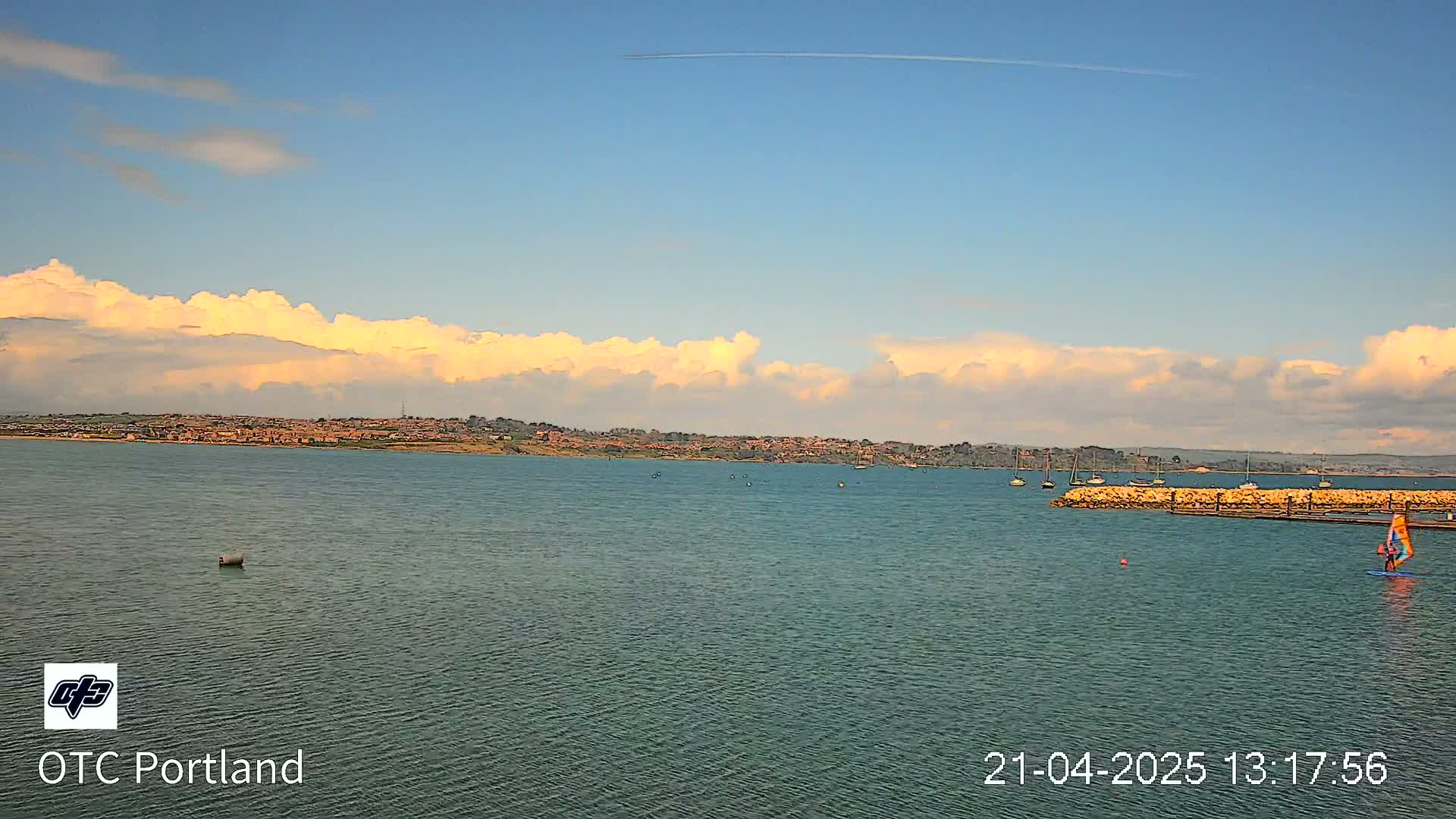 A calm body of water with a distant shoreline and a few boats under a partly cloudy sky.