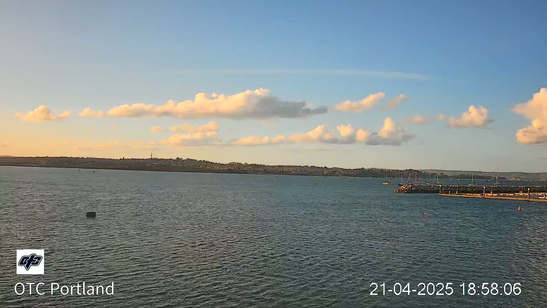A calm body of water with a distant shoreline under a partly cloudy sky at sunset.