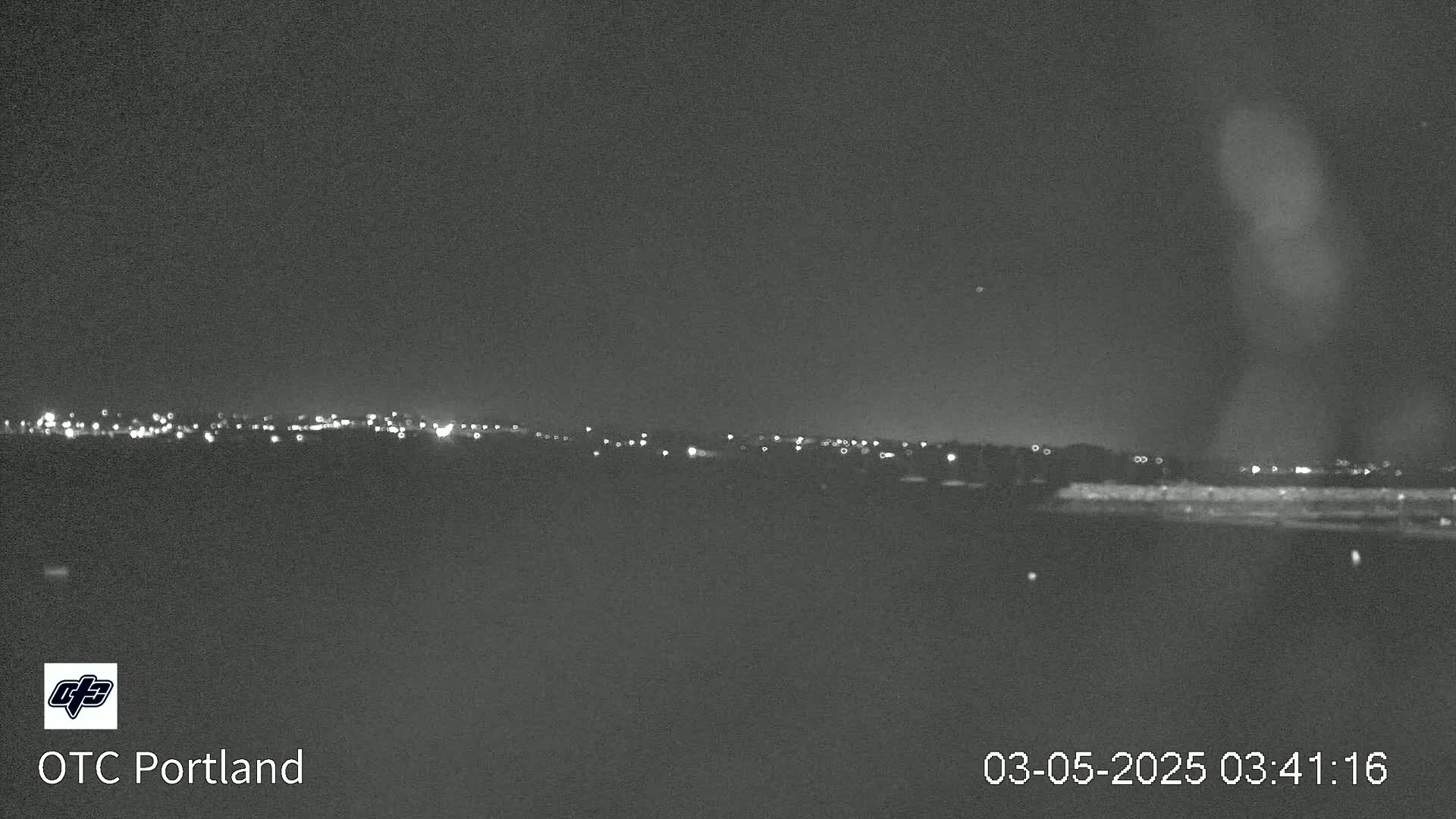 A nighttime long shot shows a distant line of city lights under a dark, clear sky.