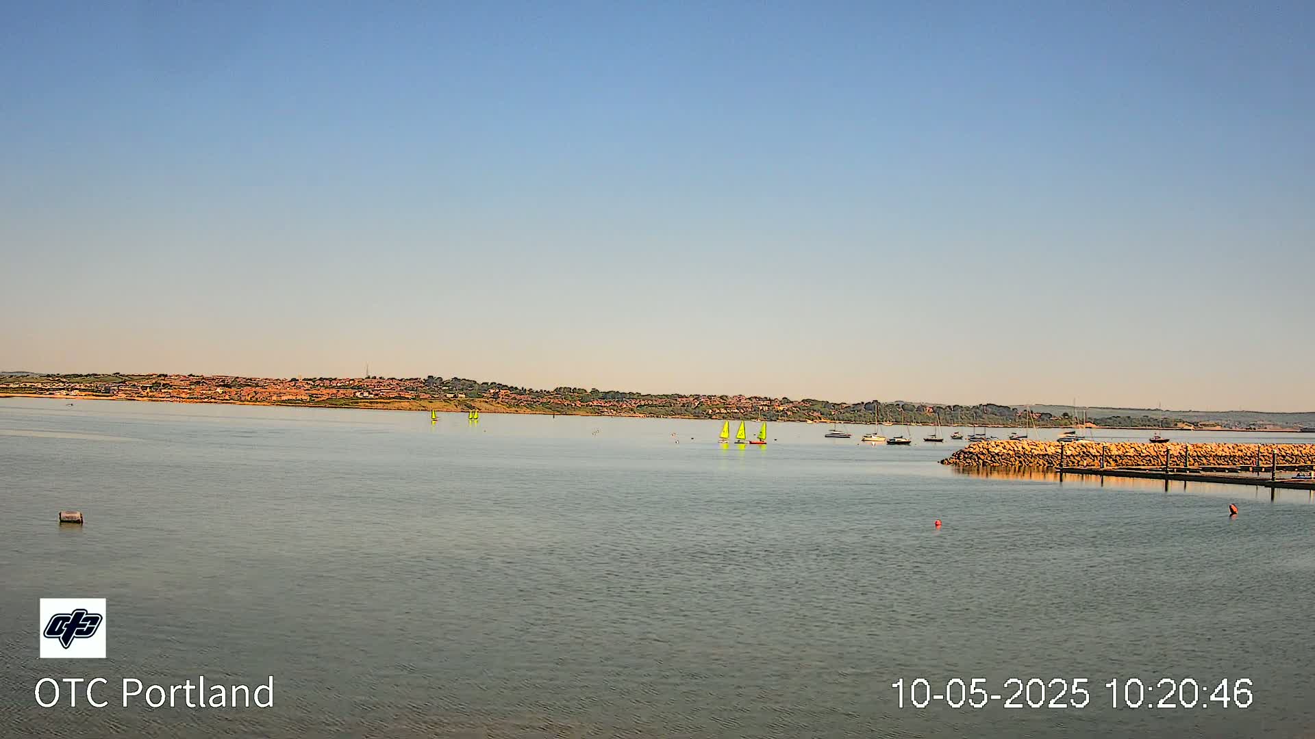 Several sailboats are visible on a calm body of water in front of a distant shoreline under a clear sky.