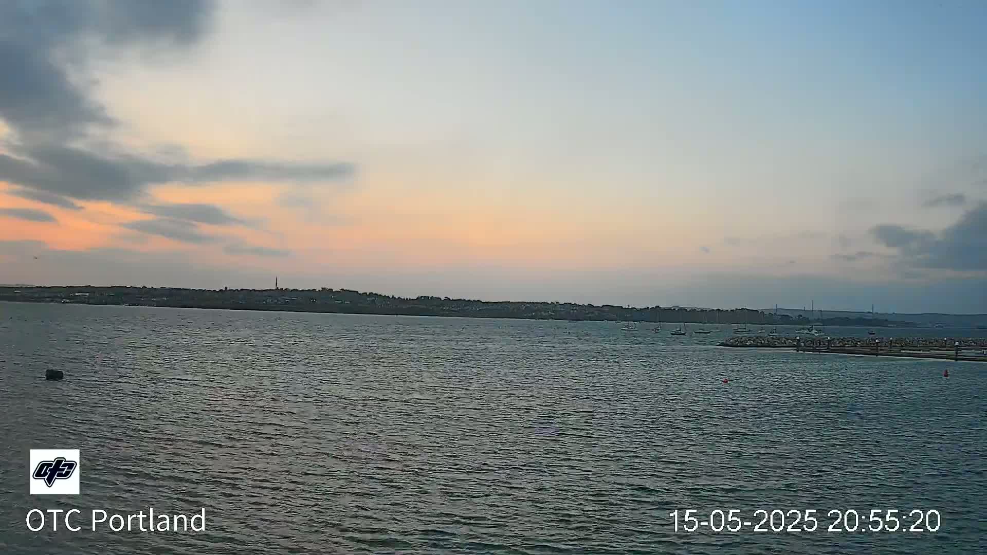 A calm body of water shows a distant shoreline at sunset under a partly cloudy sky.