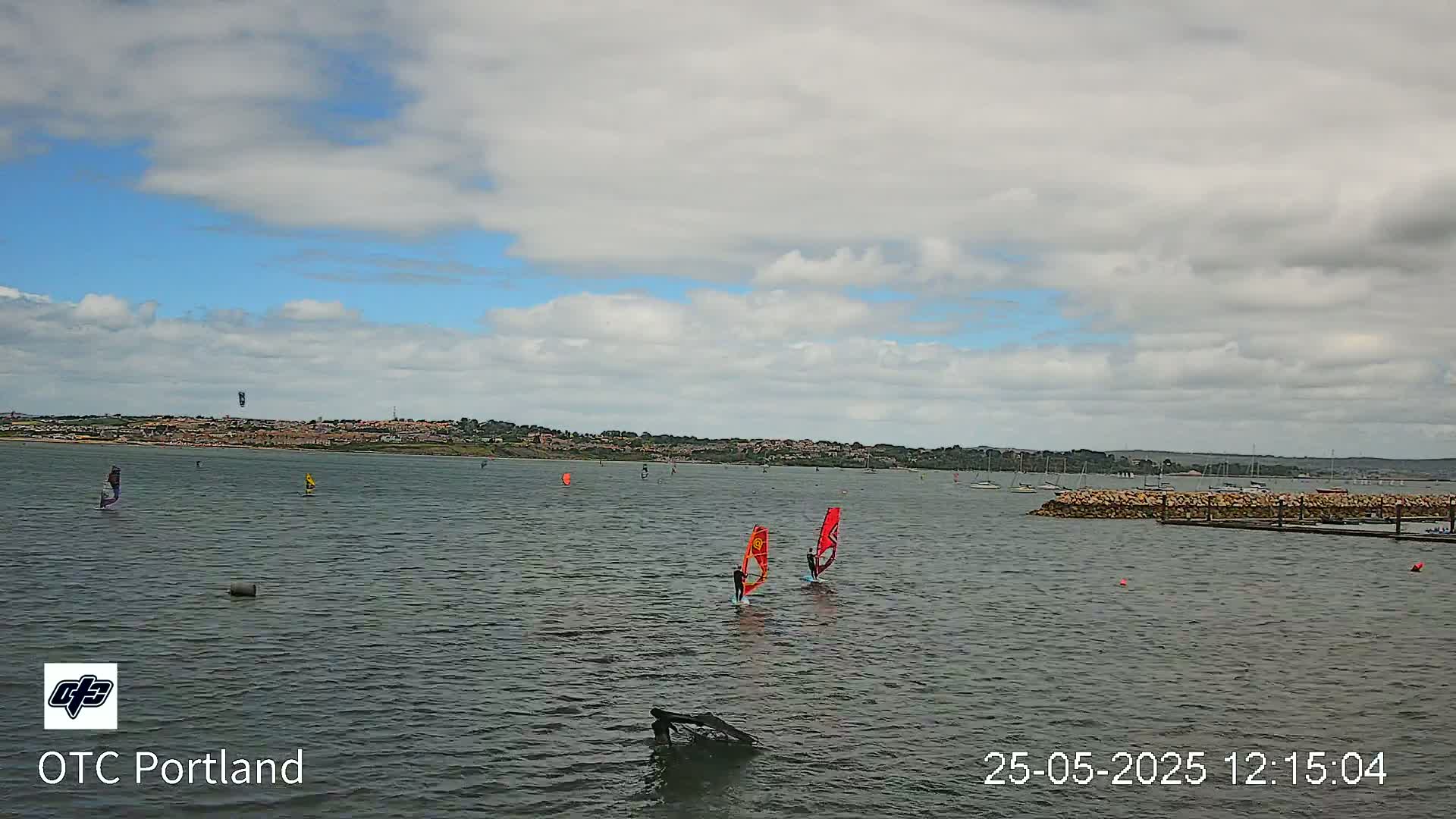 Several windsurfers are sailing on a calm body of water under a partly cloudy sky.