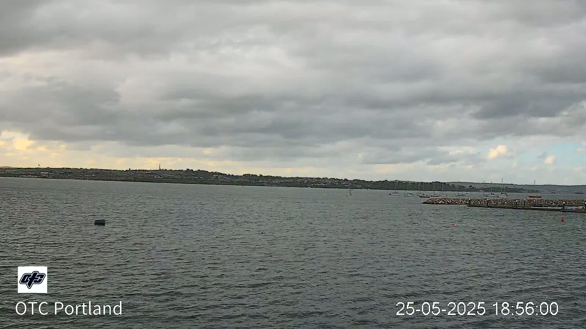 A mostly cloudy sky overlooks a calm body of water with several boats and a distant shoreline.