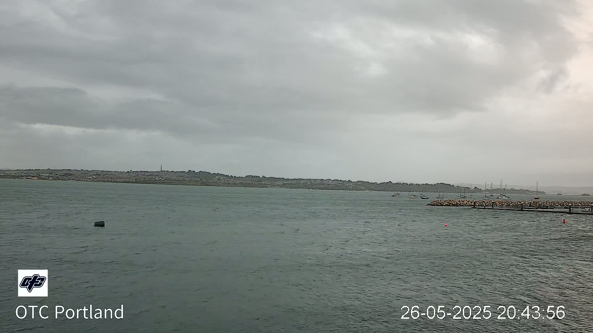 A body of water with several boats moored near a rocky shore, under a cloudy, overcast sky.