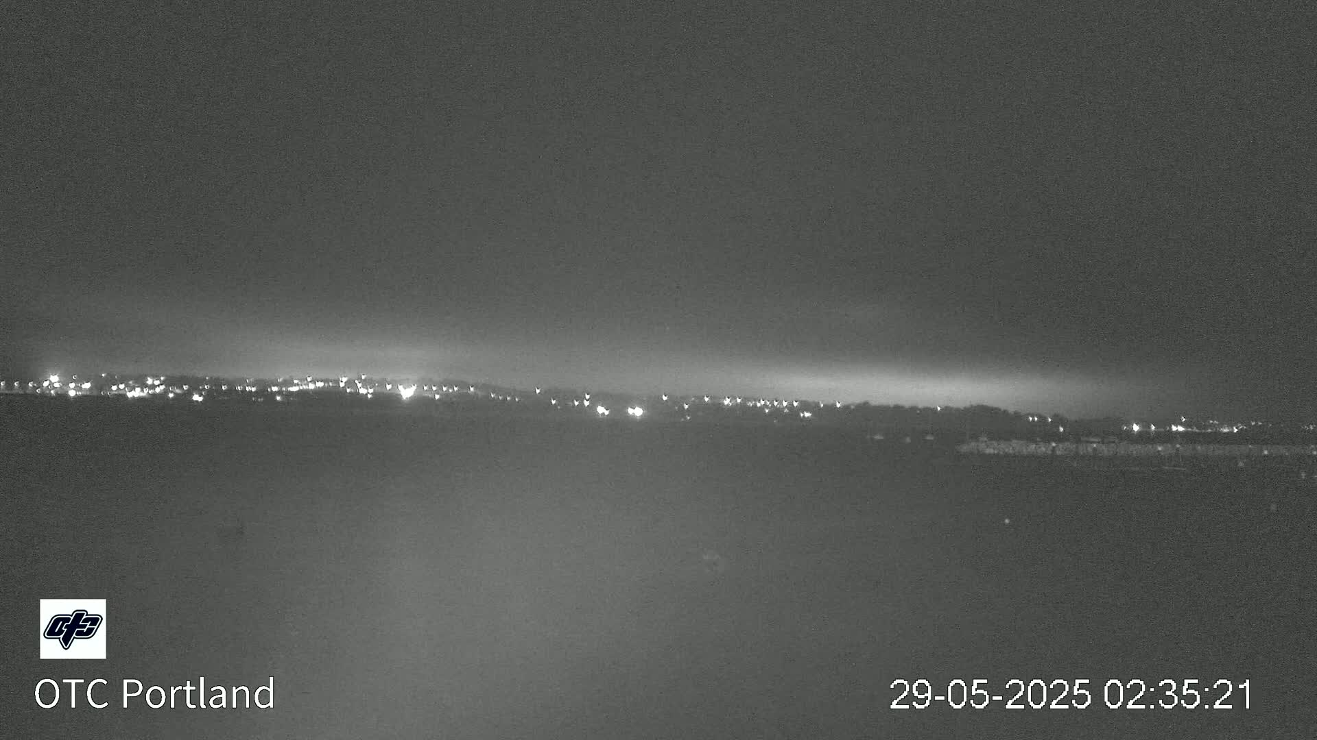A nighttime long shot shows a distant line of city lights under a dark, overcast sky.