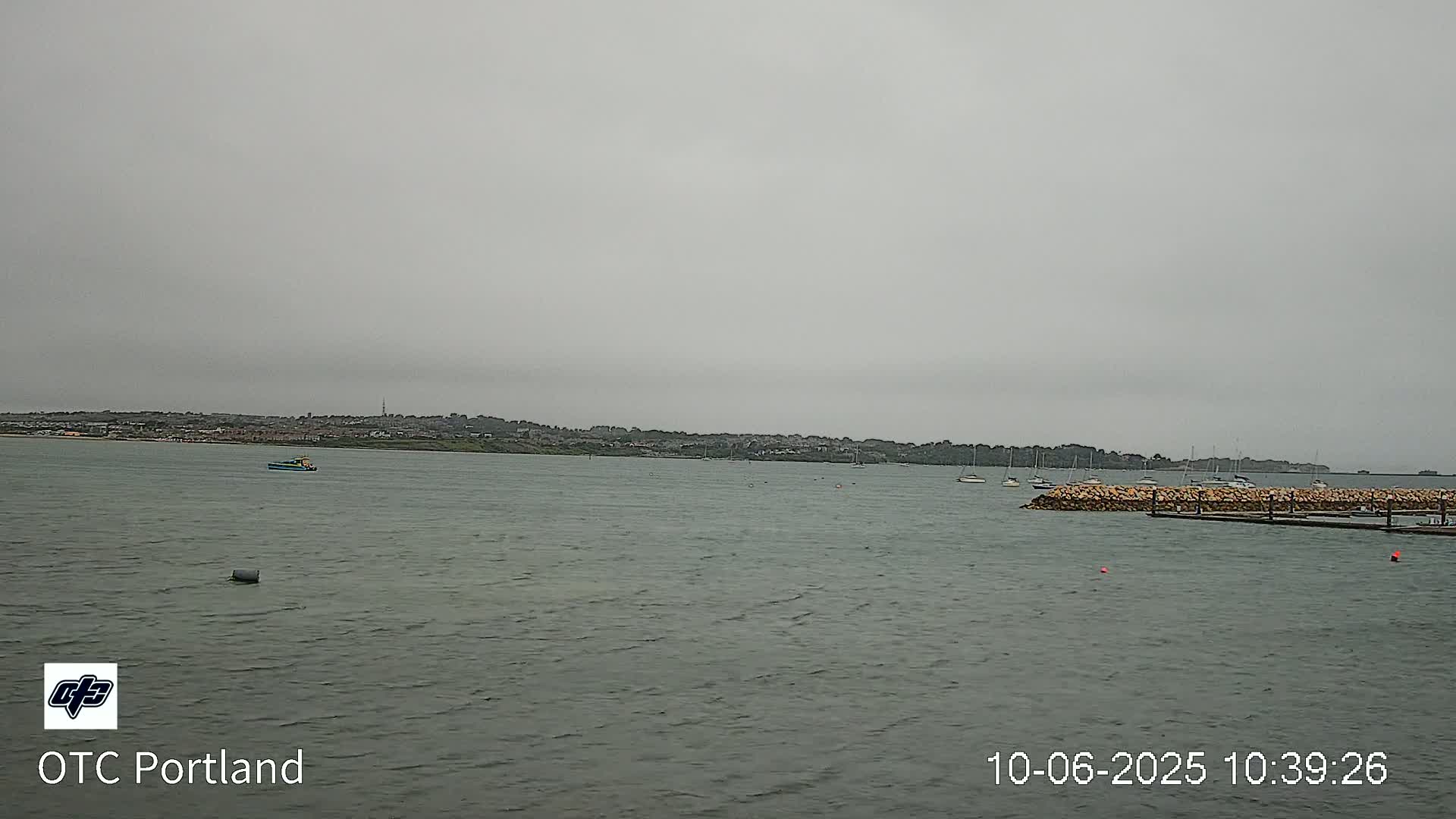 A calm body of water shows several small boats and a distant shoreline under an overcast sky.