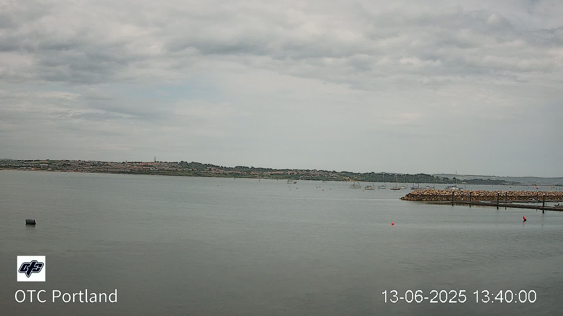 A calm body of water with a few boats and a distant shoreline under an overcast sky.