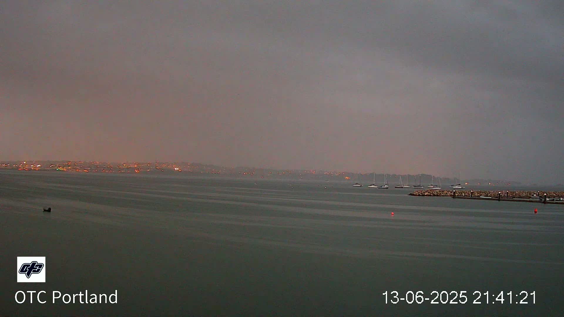A calm body of water shows a distant, dimly lit shoreline under an overcast sky.
