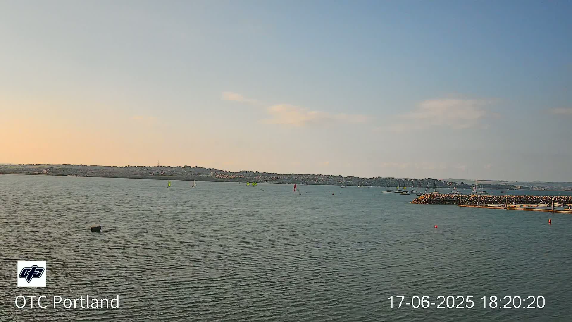 A calm body of water with several sailboats and a distant shoreline under a mostly clear sky.
