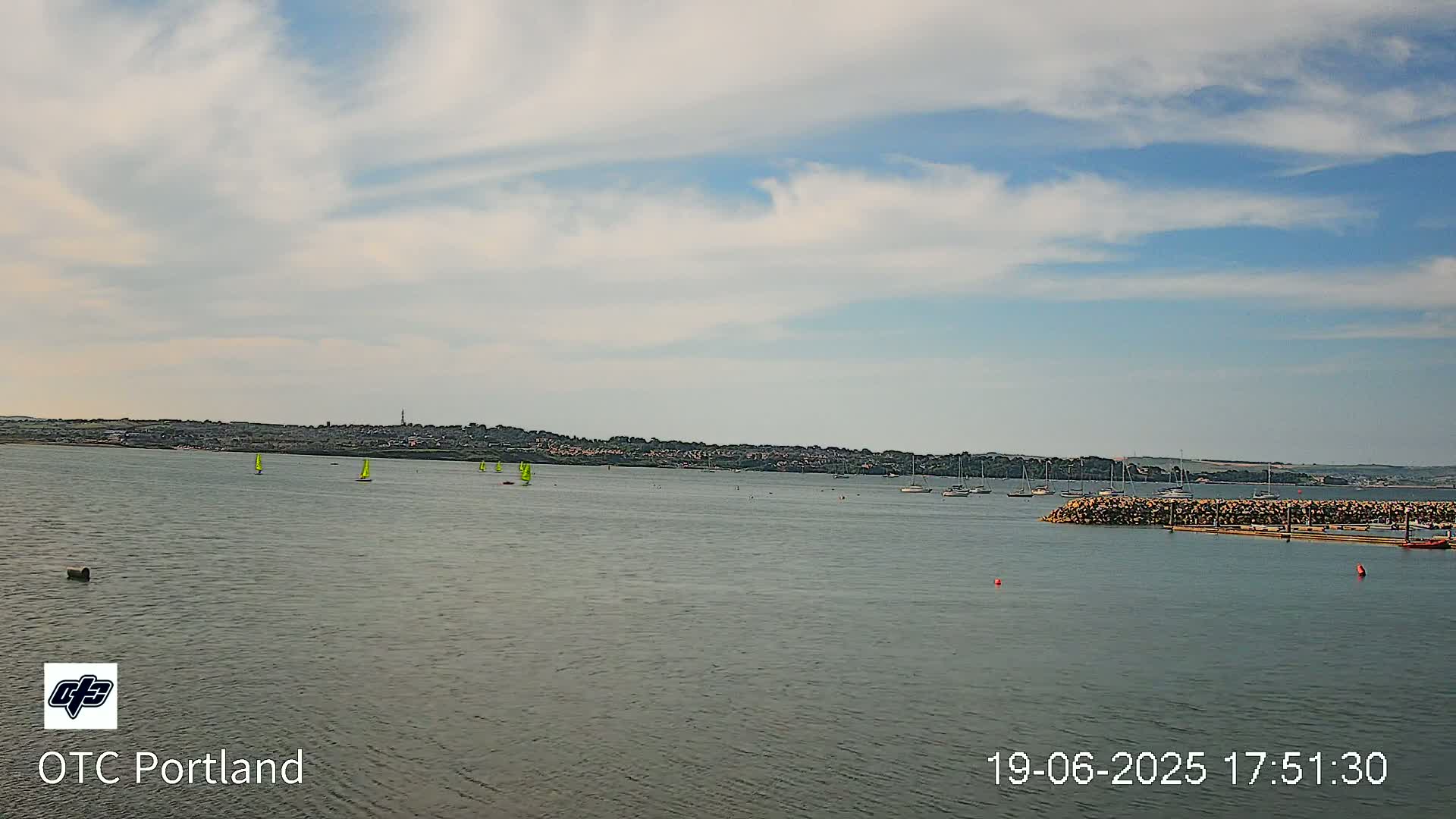 A calm body of water with several sailboats and a distant shoreline under a partly cloudy sky.