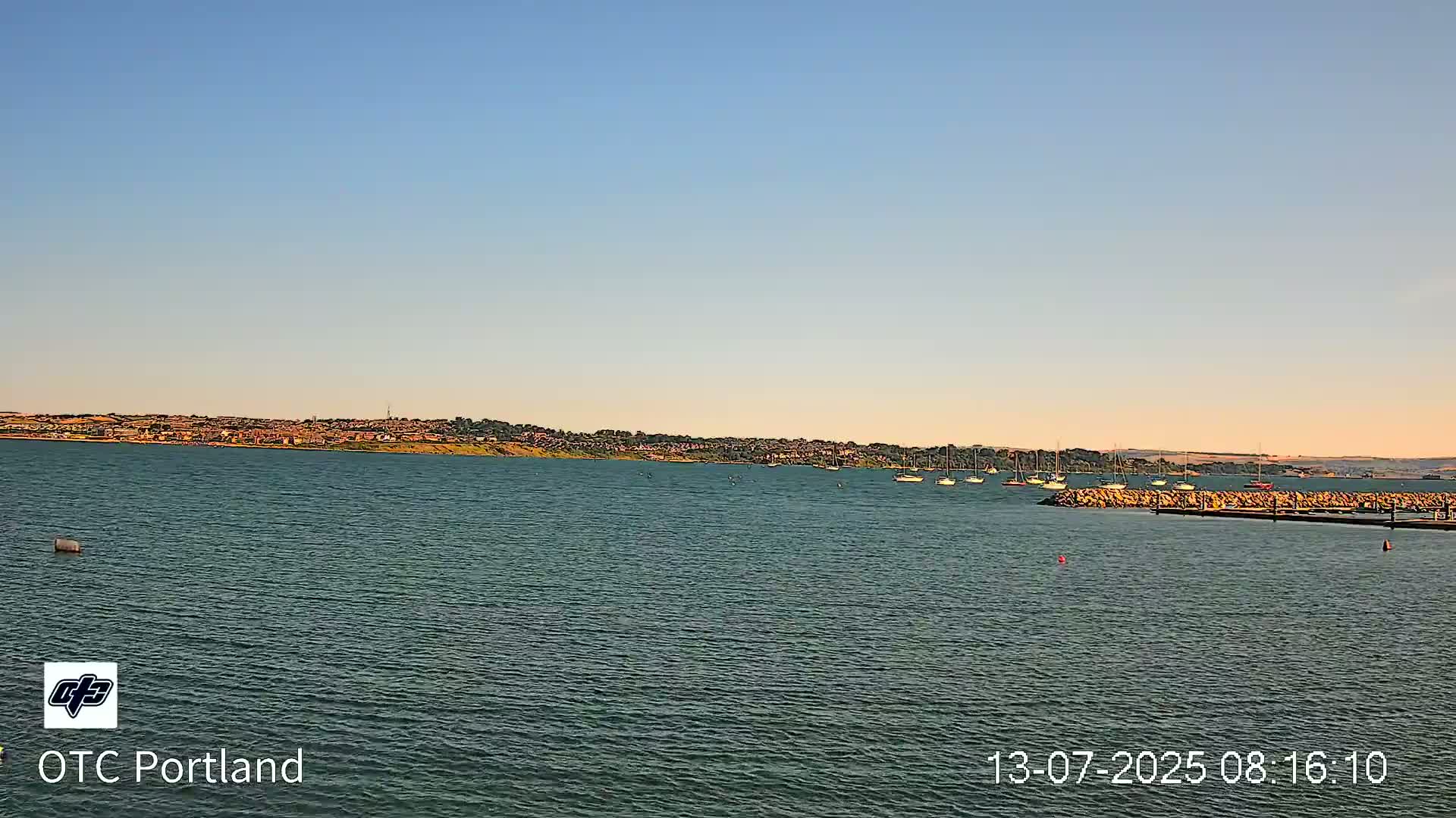 A calm body of water with several sailboats and a distant shoreline under a clear blue sky.