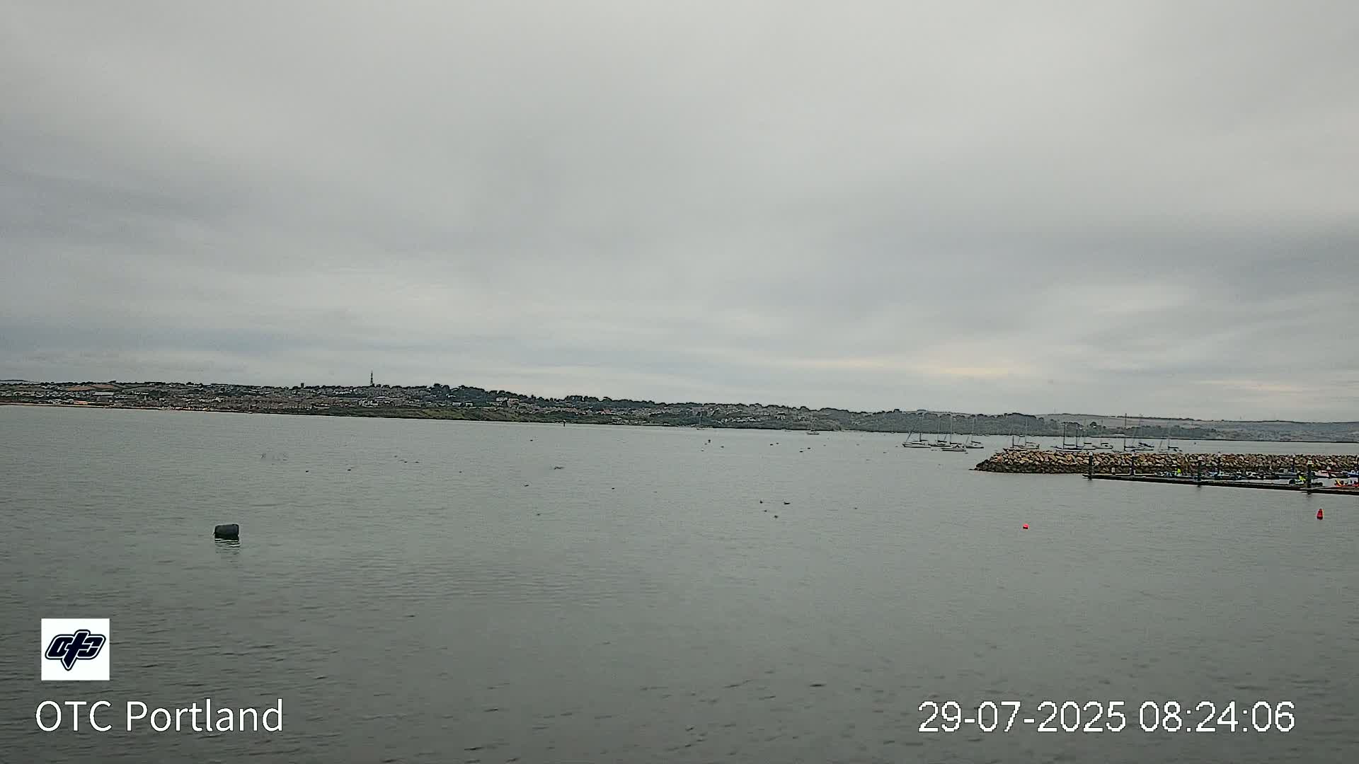 A calm body of water stretches out to a distant town under an overcast sky.