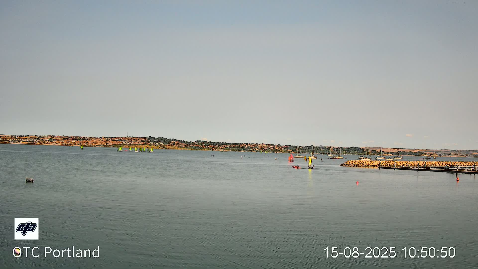 A calm body of water stretches out to a distant town under an overcast sky.