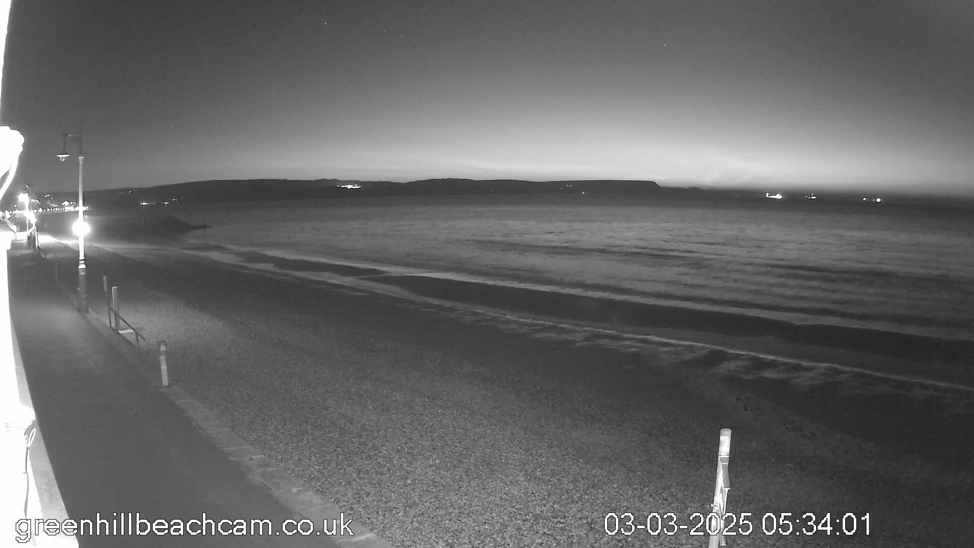 A dark, pebble beach stretches to a calm sea under a twilight sky.