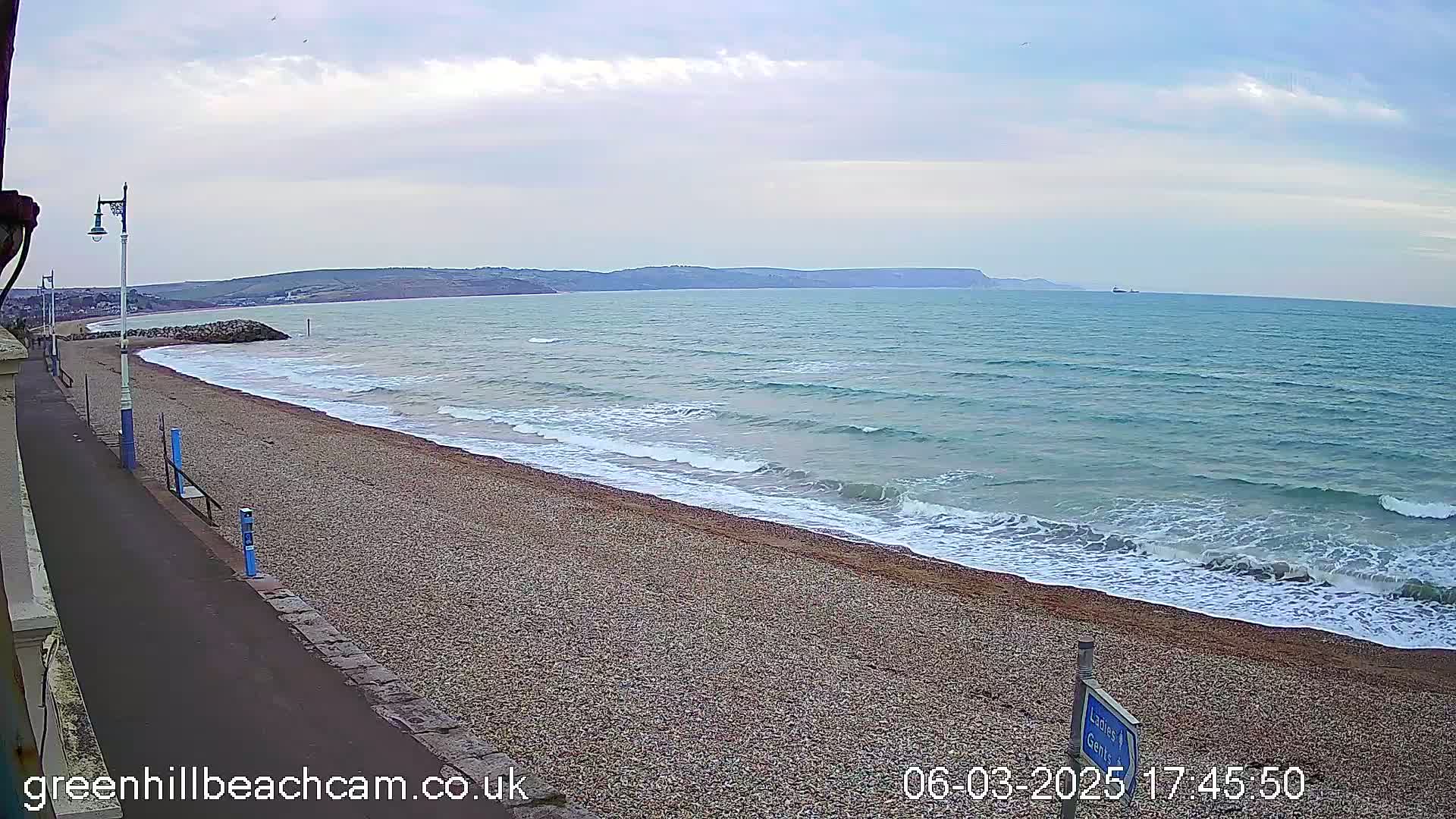 A pebble beach with gentle waves rolling onto the shore under a cloudy sky.