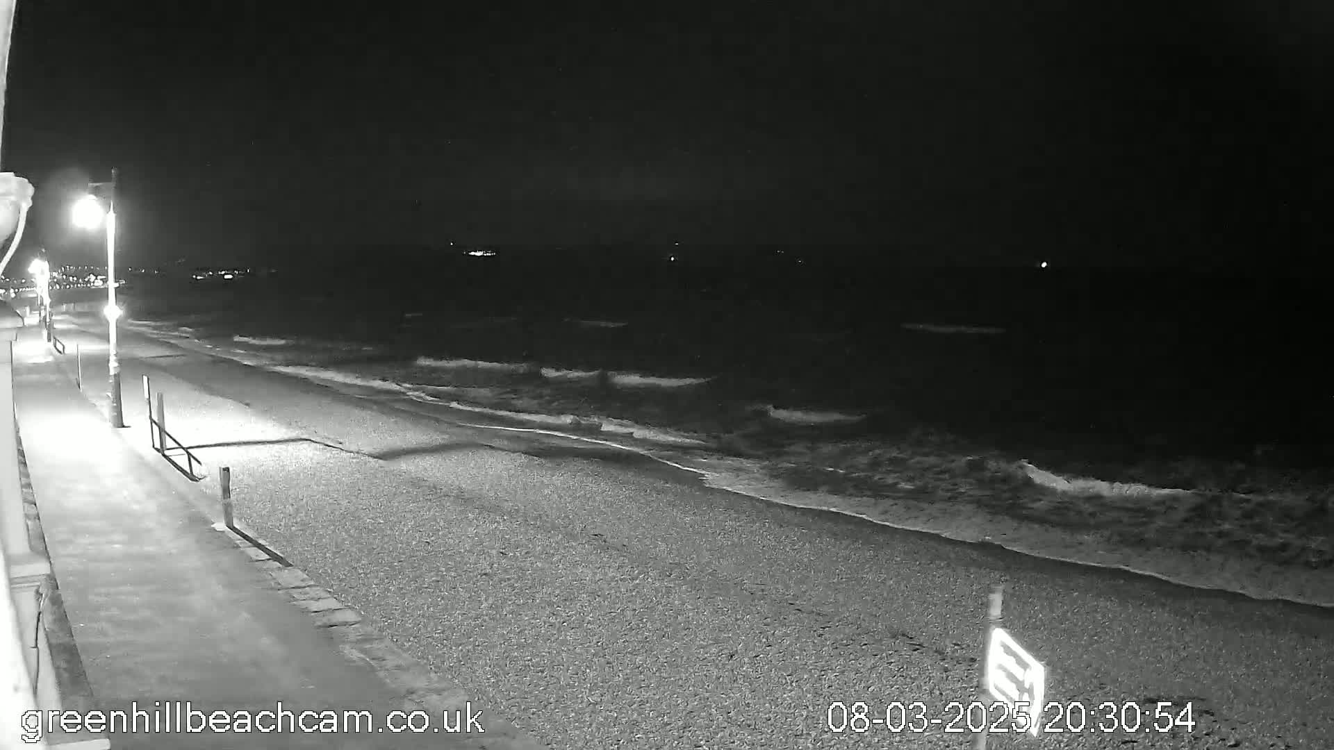 A nighttime view of a pebble beach with gently lapping waves under a dark sky.