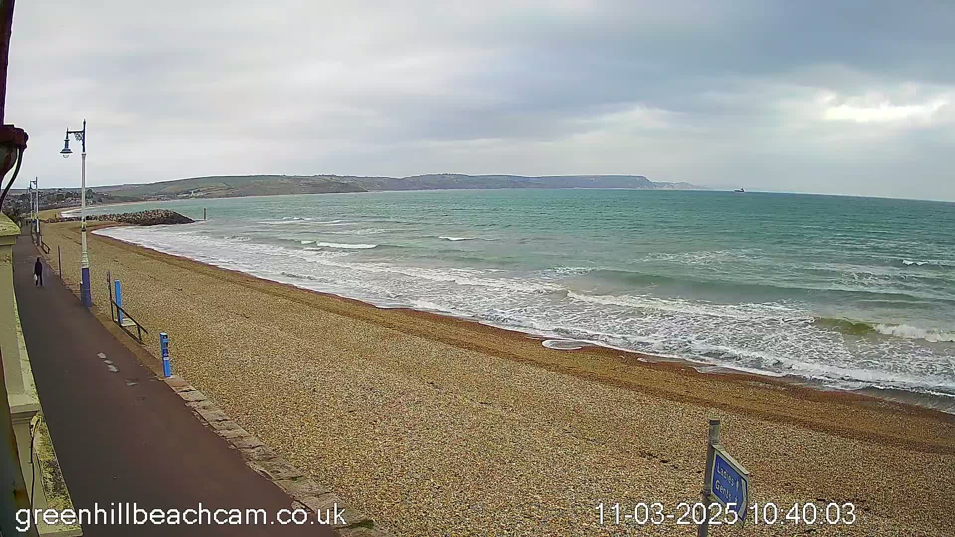 A pebble beach with gentle waves rolling onto the shore under an overcast sky.