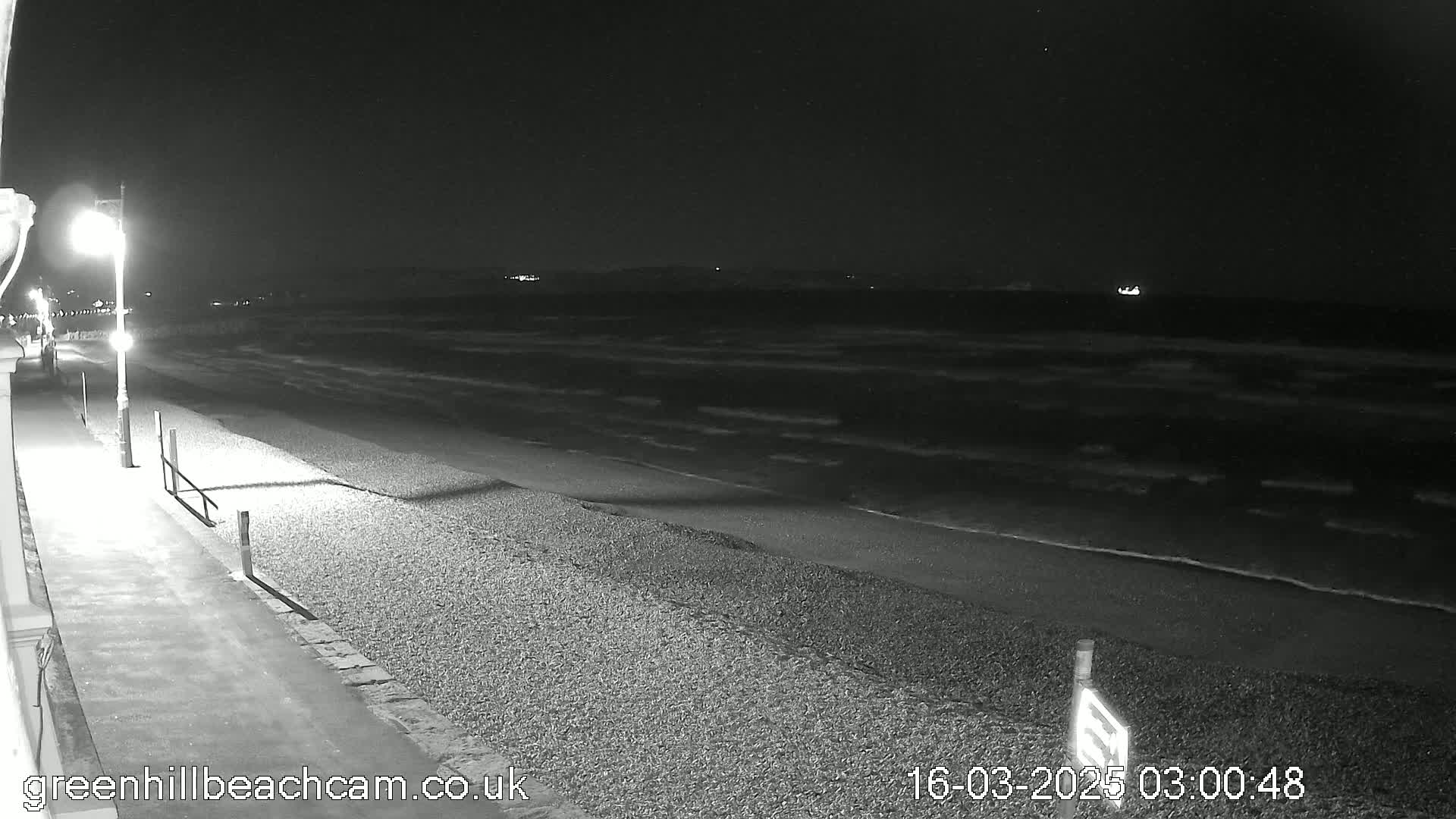 A nighttime view of a pebble beach with gentle waves lapping the shore under a dark sky.