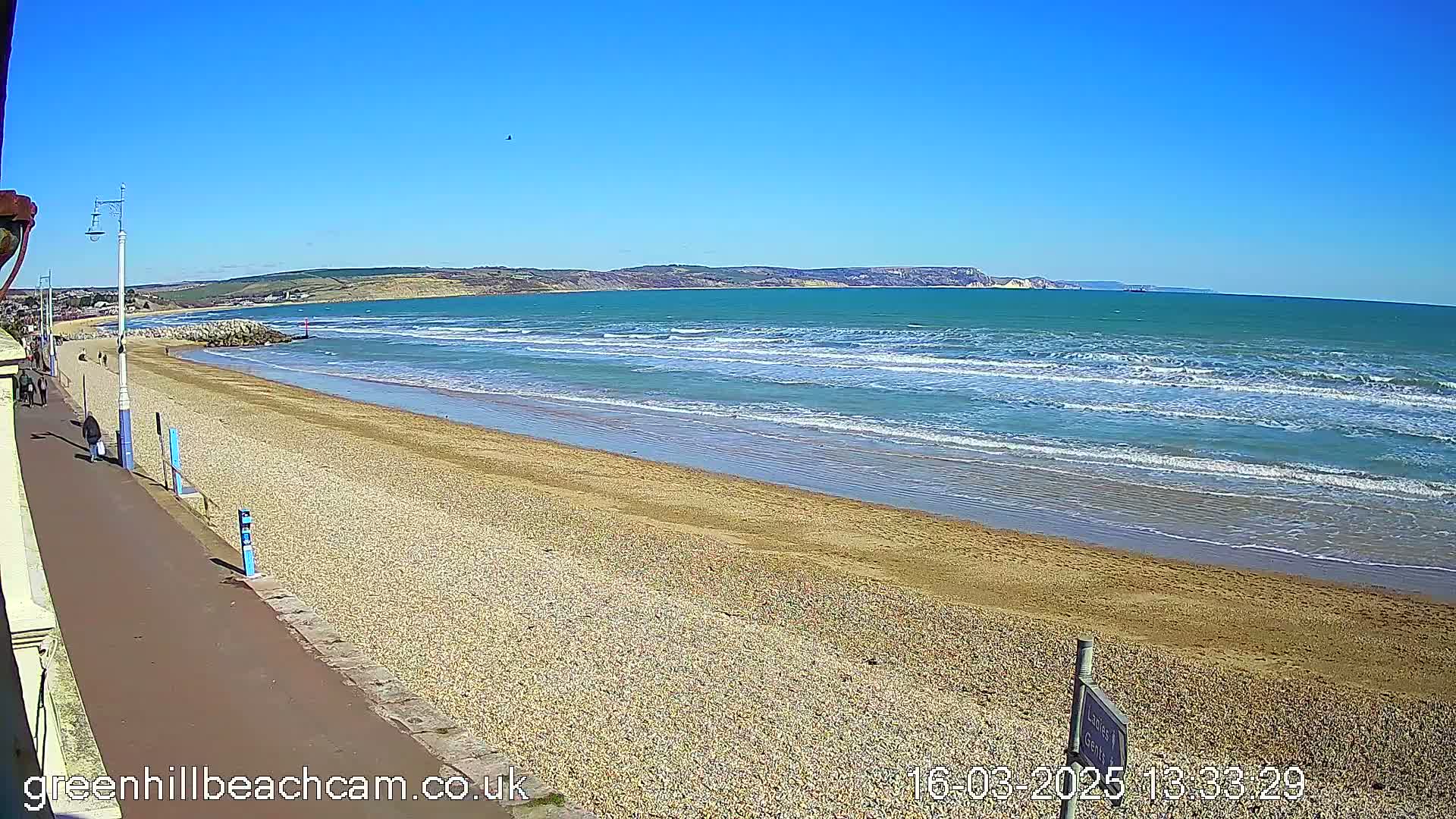 A sandy beach with small waves under a clear blue sky stretches toward a distant coastline.