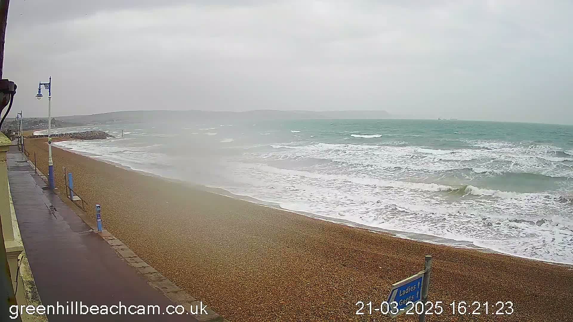 A pebble beach with moderate waves crashing on the shore under an overcast sky.