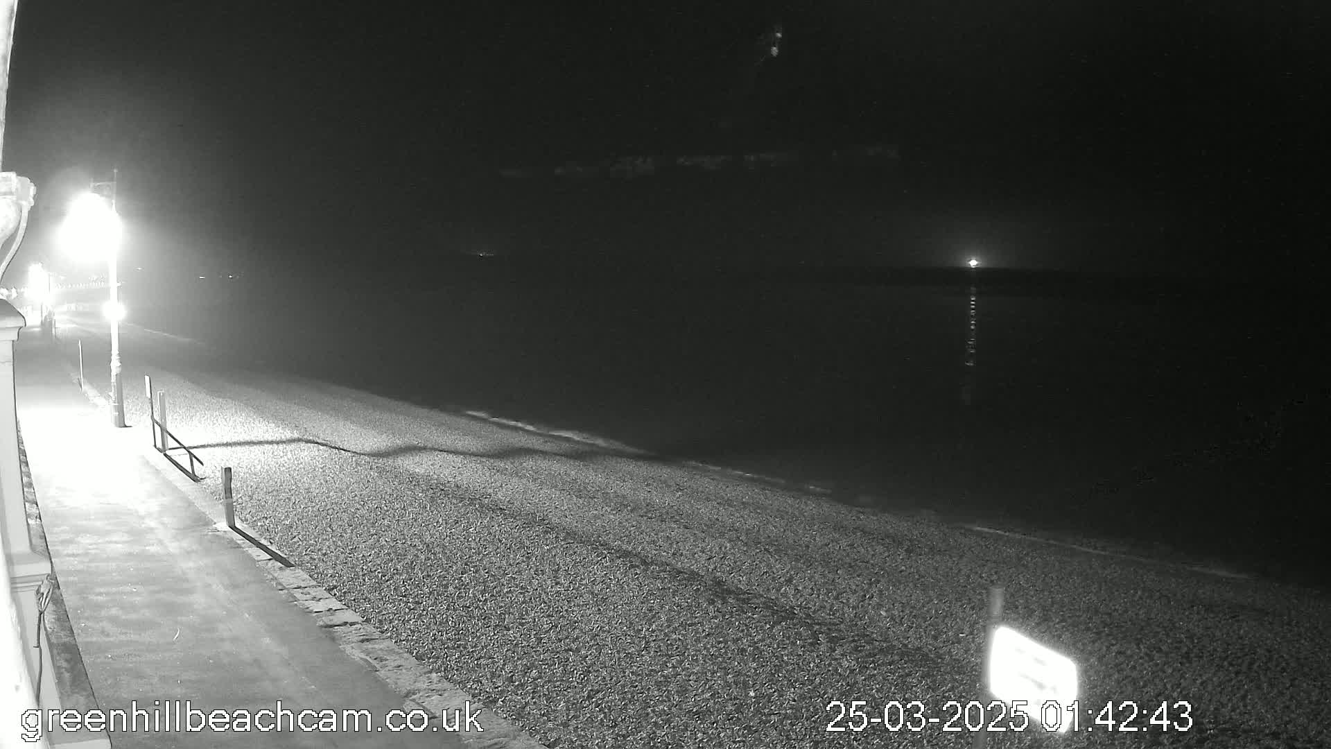 A nighttime, low-light view of a pebble beach and calm water under a clear, dark sky.