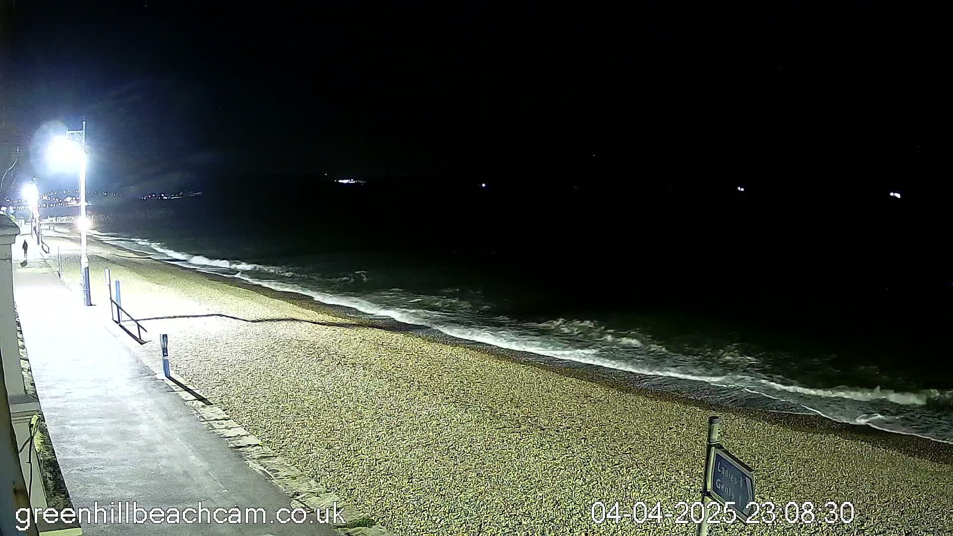A nighttime view of a pebble beach with gentle waves lapping the shore under a dark sky.