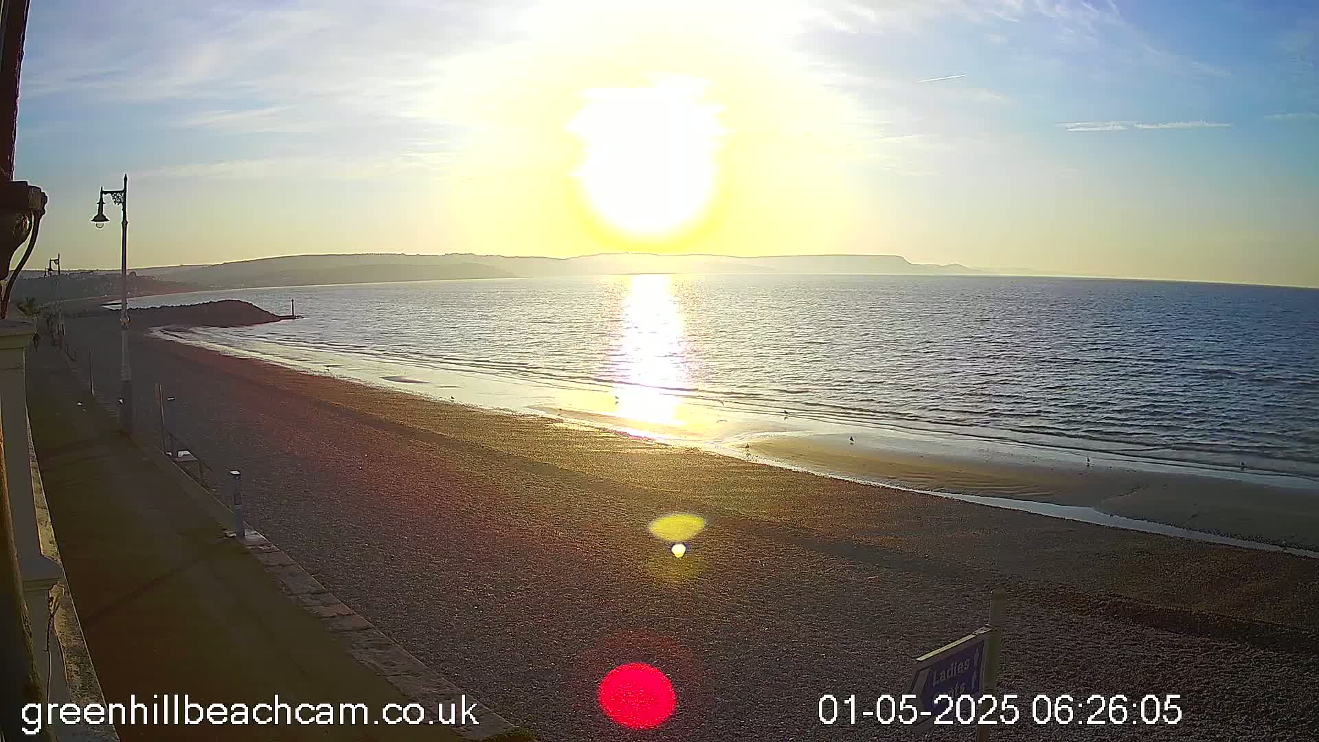 A sandy beach stretches toward a calm sea under a bright sunset.